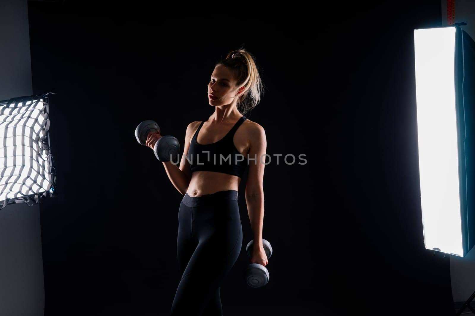 Athletic woman in a sportswear raises dumbbells leads healthy lifestyle has happy expression
