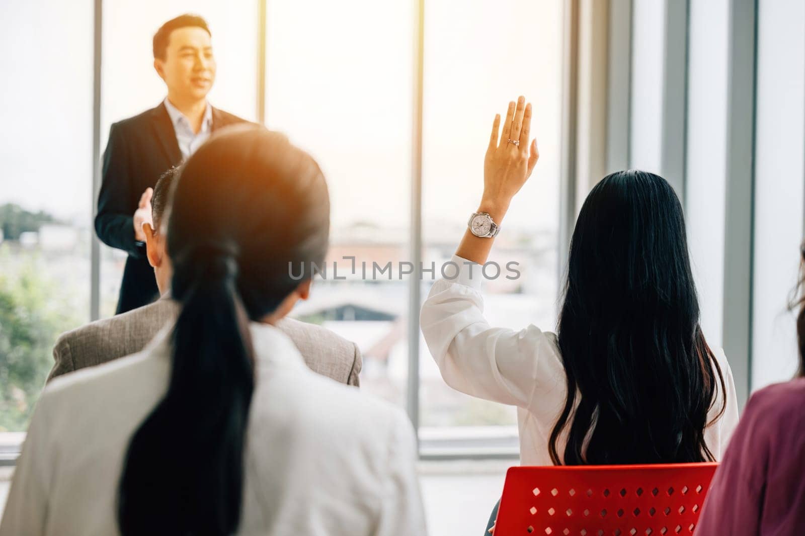 A diverse crowd in a corporate event raises their hands for questions, voting, or volunteering, emphasizing teamwork and audience interaction during the conference. by Sorapop
