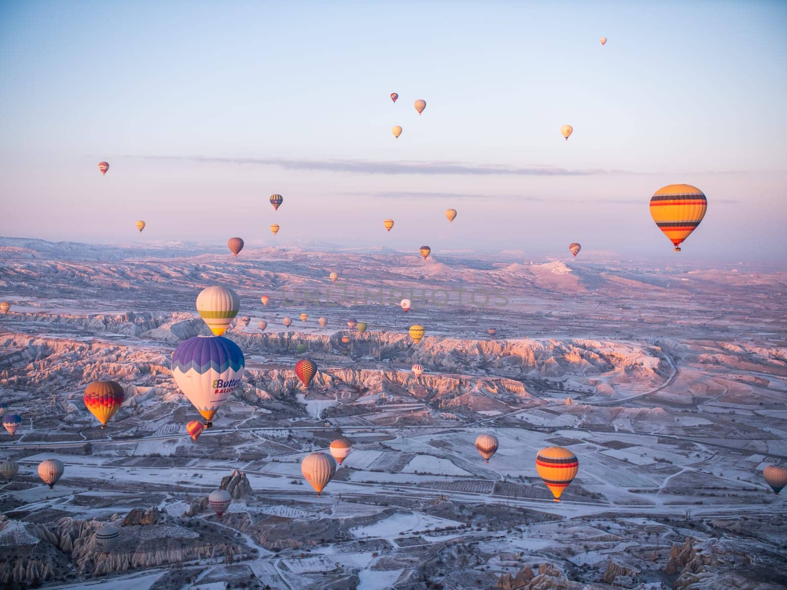 Goreme, Turkey - January 11, 2020: Colorful balloons over volcanic rocks in Cappadocia. Turkey. by DovidPro