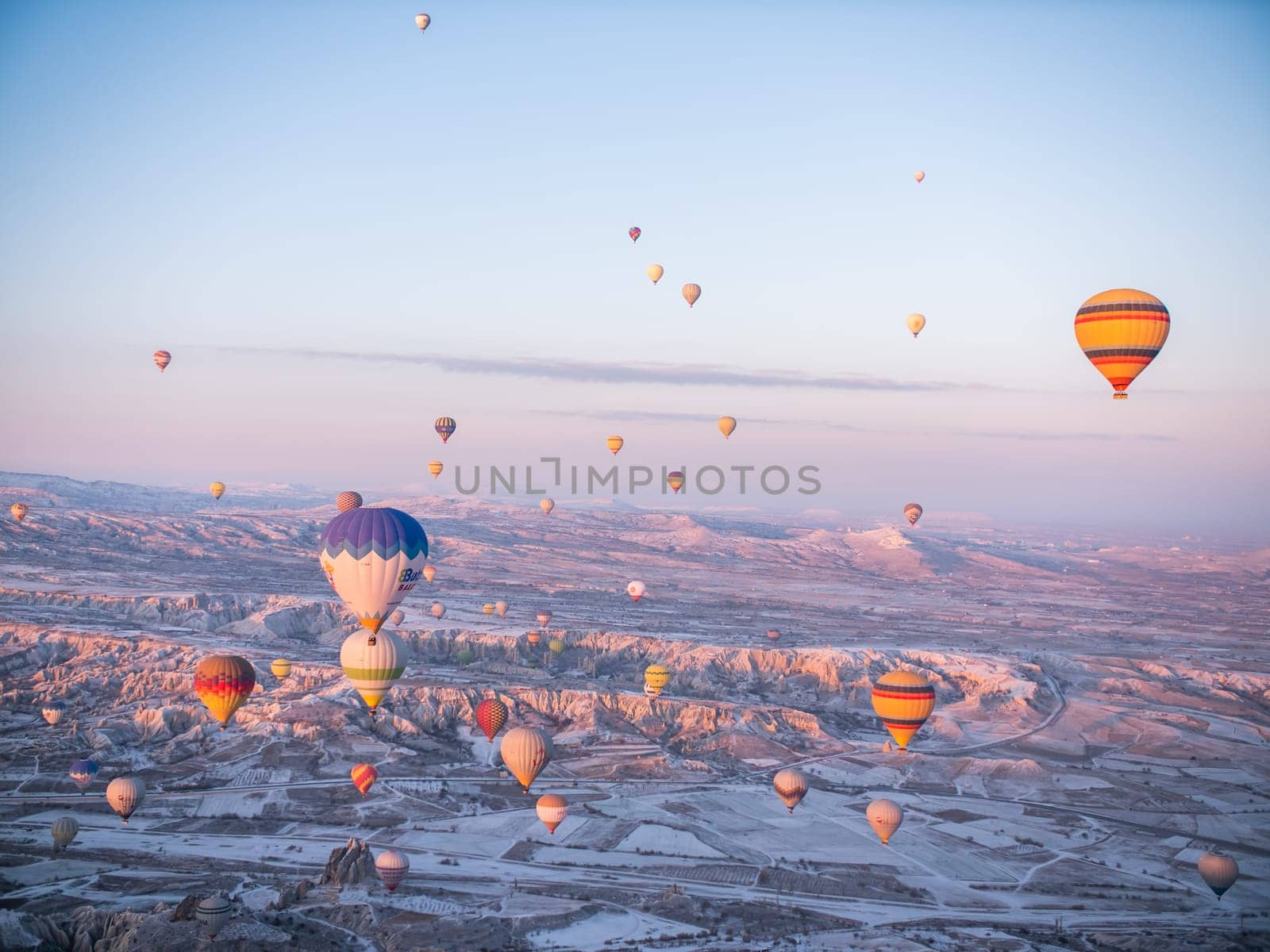 Goreme, Turkey - January 11, 2020: Colorful balloons over volcanic rocks in Cappadocia. Turkey. by DovidPro