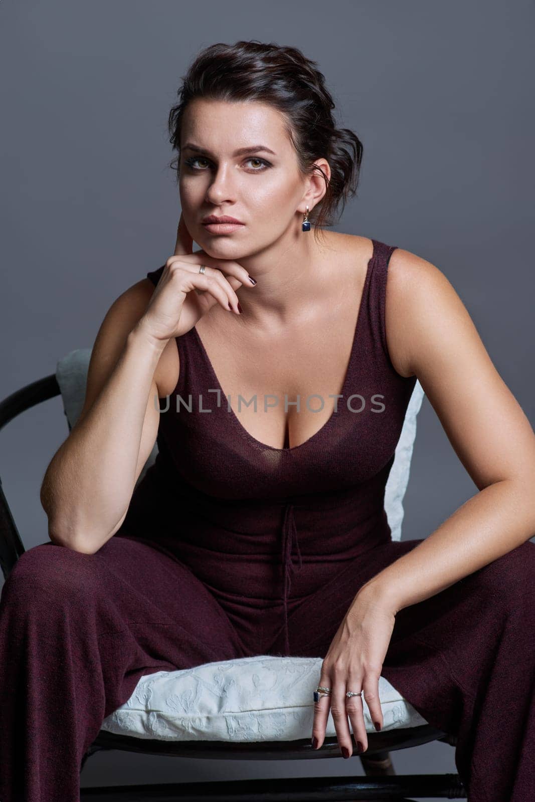 Fashionable sensual attractive young woman posing sitting in chair on dark gray studio background. Beauty, fashion, style concept