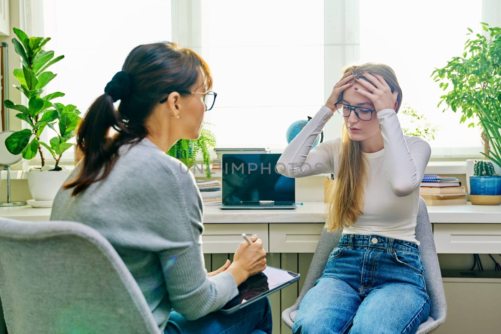 Young female teenager 16, 17 years old talking with counselor psychologist behavior social worker teacher, sitting in chair in office. Psychology psychotherapy therapy mental health adolescence youth