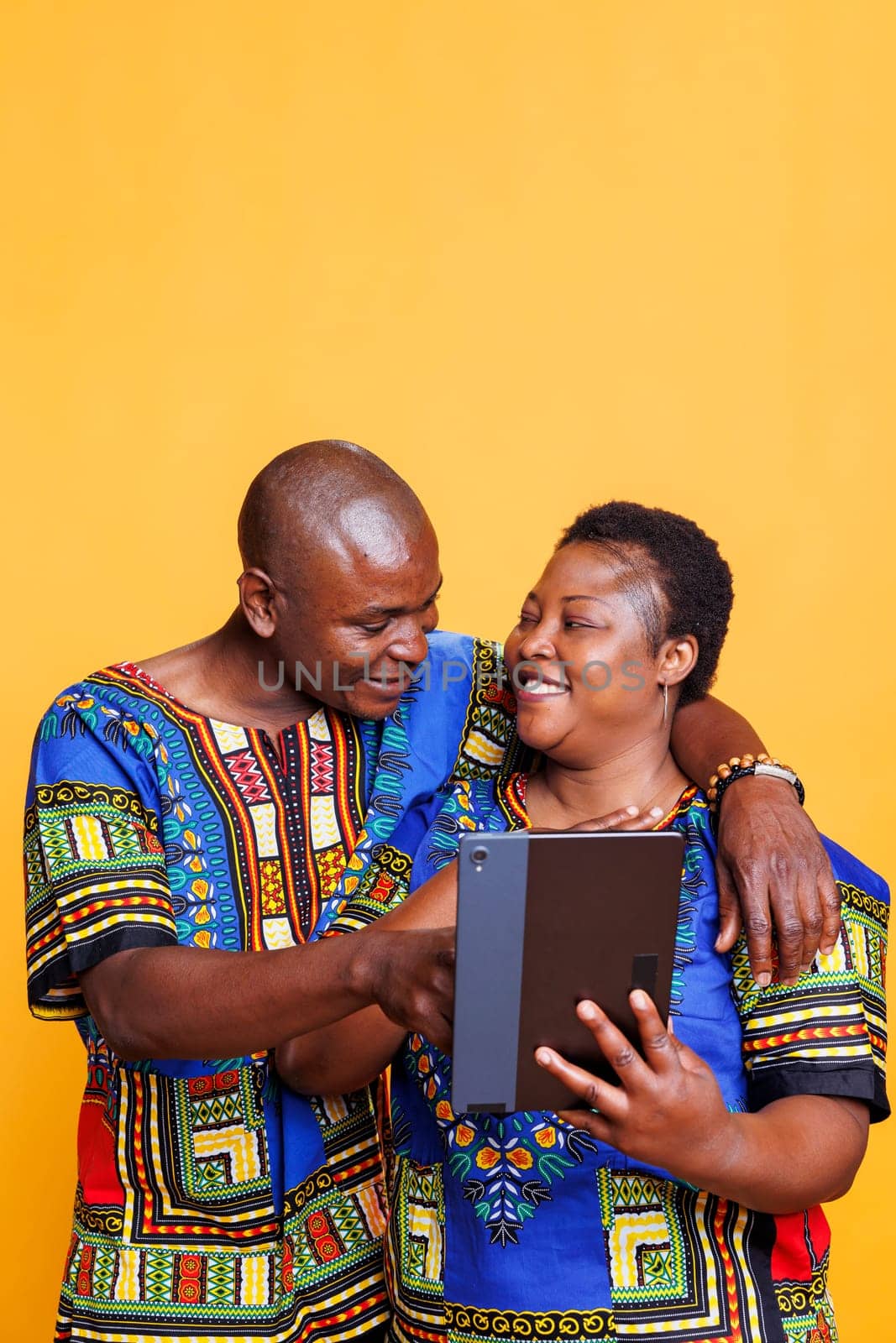 Happy african american couple in love embracing while using digital tablet together. Cheerful mature boyfriend and girlfriend tapping on device touchscreen and scrolling internet page