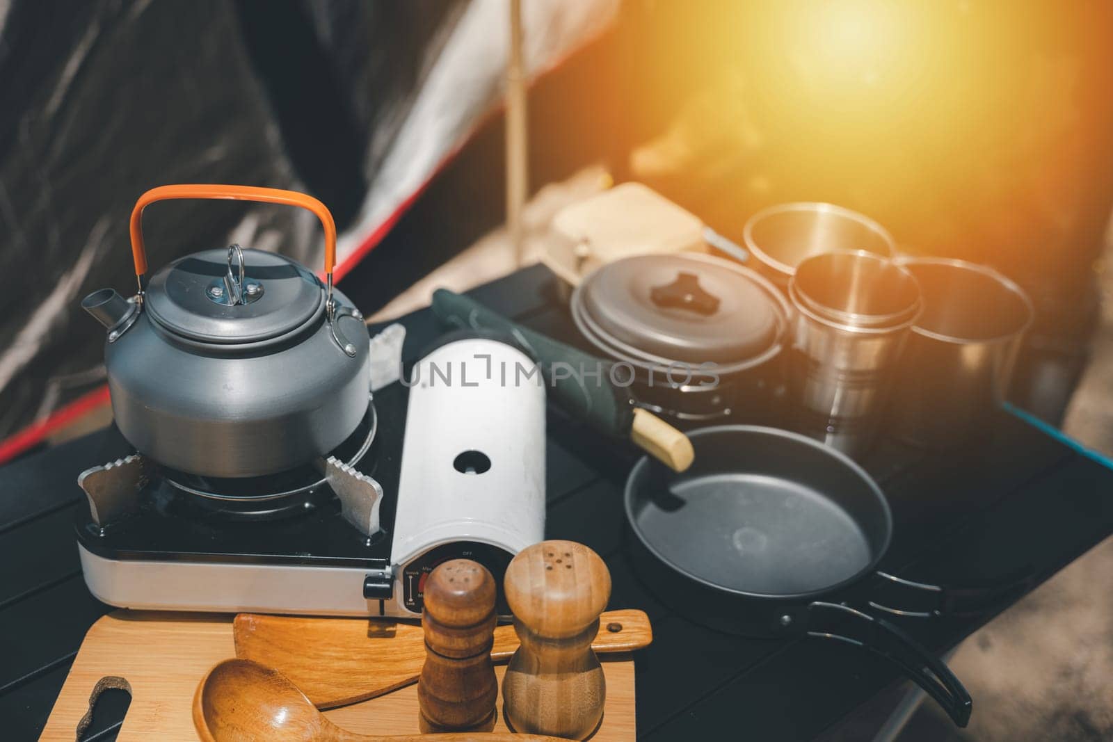 Enhance your camping adventure, kettle, pot, pan, gas stove, flashlight, and camera neatly set on a table by the tent. The perfect outdoor setup for a memorable journey. by Sorapop