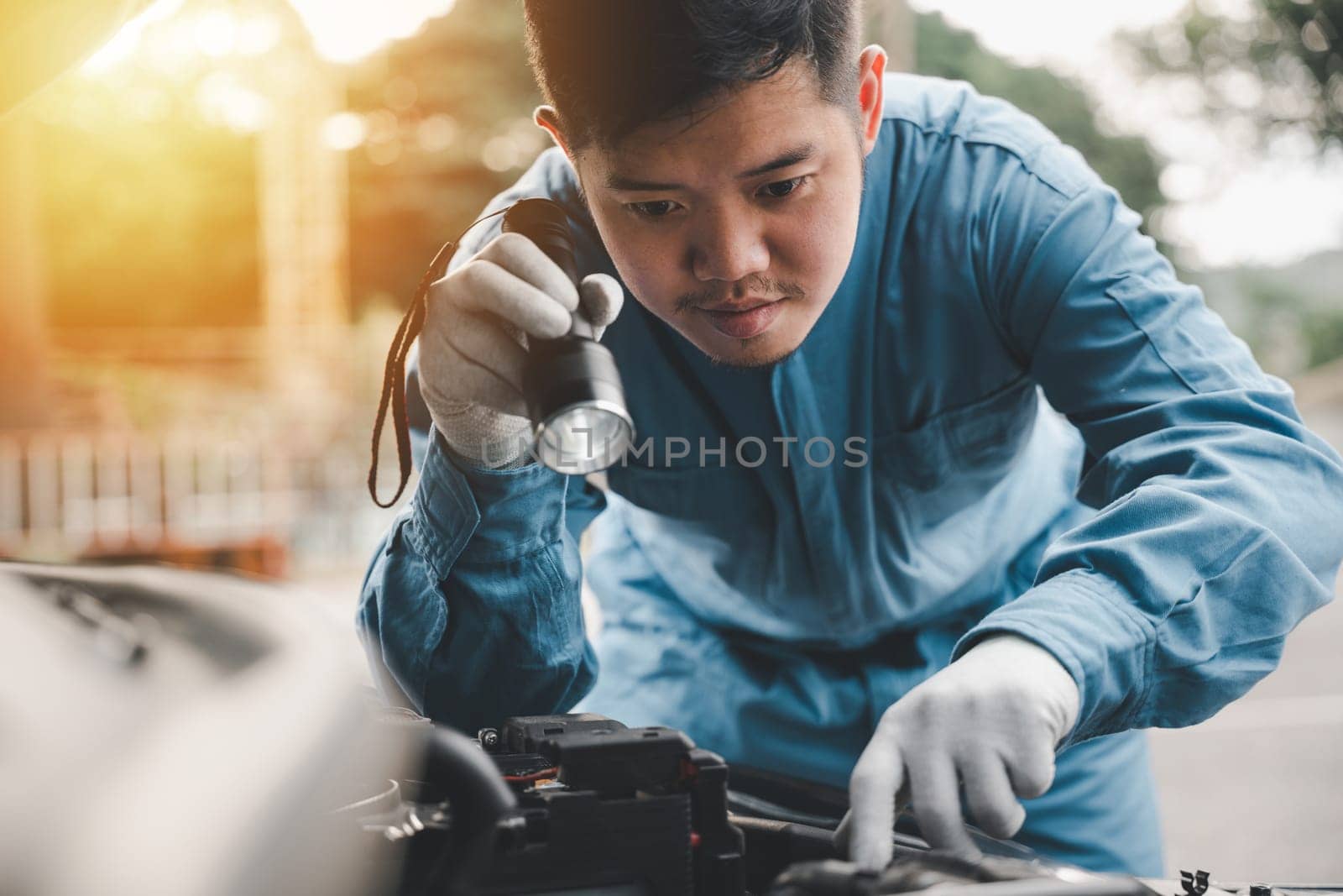 Car mechanic service technician analyzing auto engine problems with an electric lamp on the cradle. Expert repairing a car in the workshop.