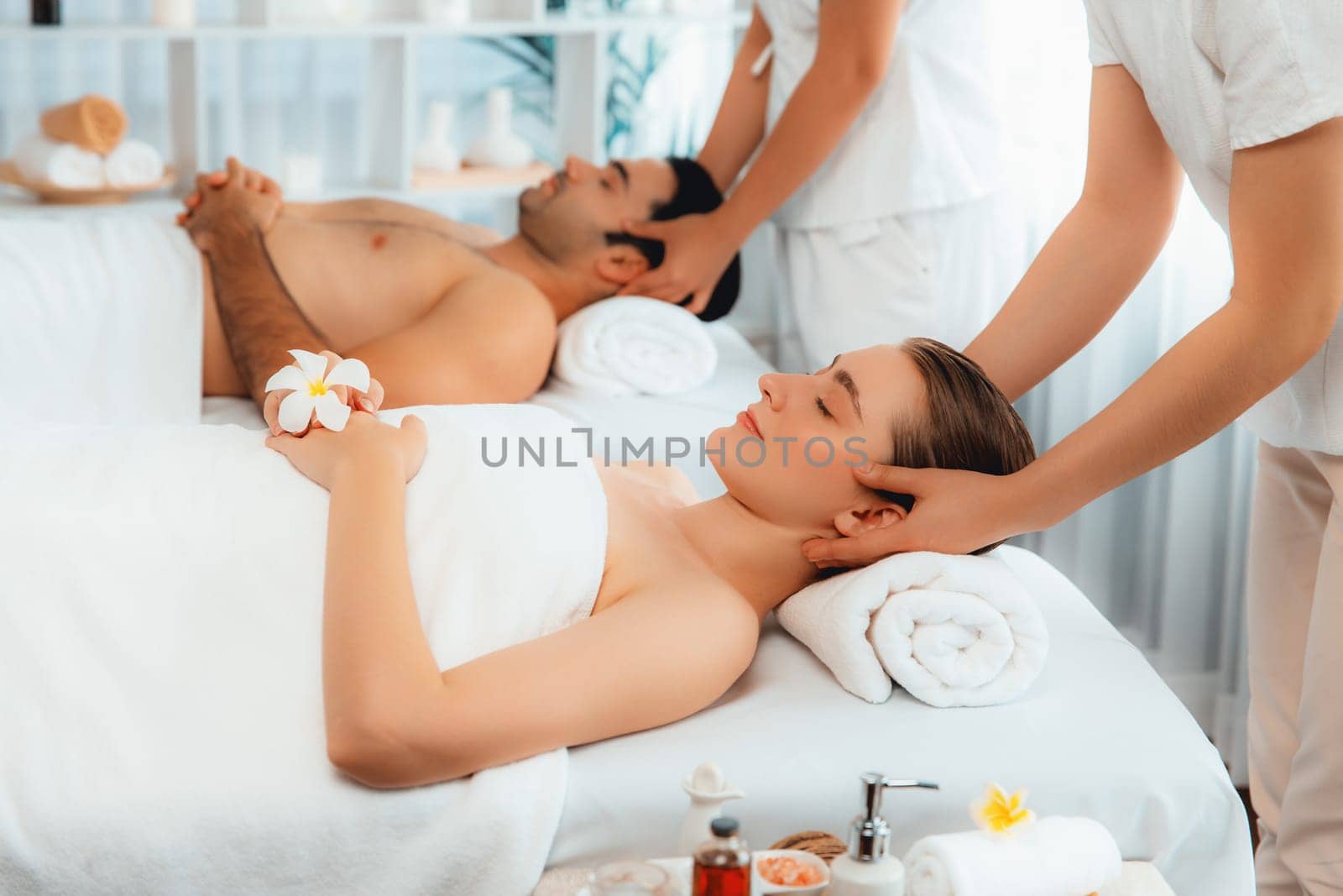 Caucasian couple enjoying relaxing anti-stress head massage and pampering facial beauty skin recreation leisure in dayspa modern light ambient at luxury resort or hotel spa salon. Quiescent