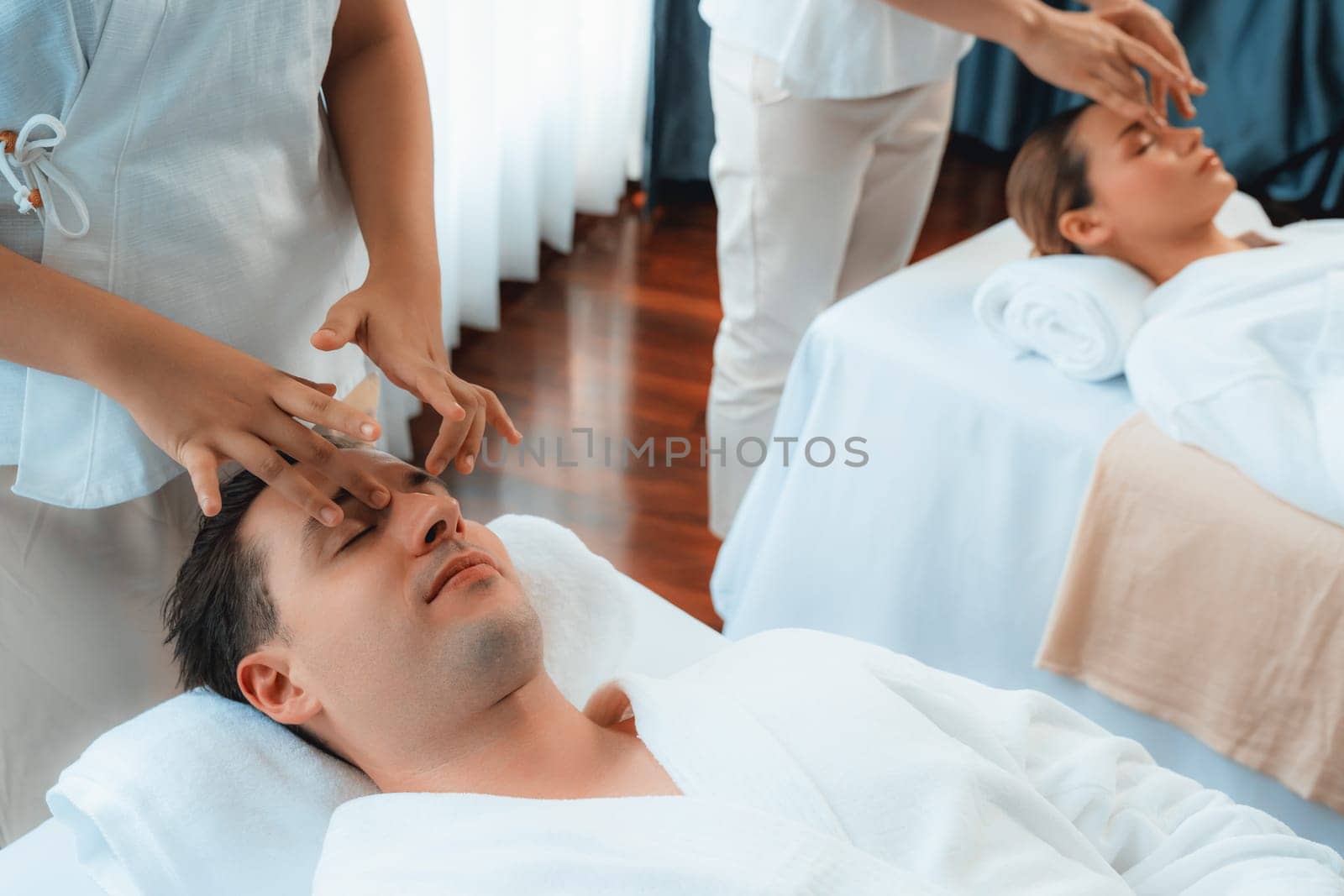 Caucasian couple enjoying relaxing anti-stress head massage and pampering facial beauty skin recreation leisure in dayspa modern light ambient at luxury resort or hotel spa salon. Quiescent