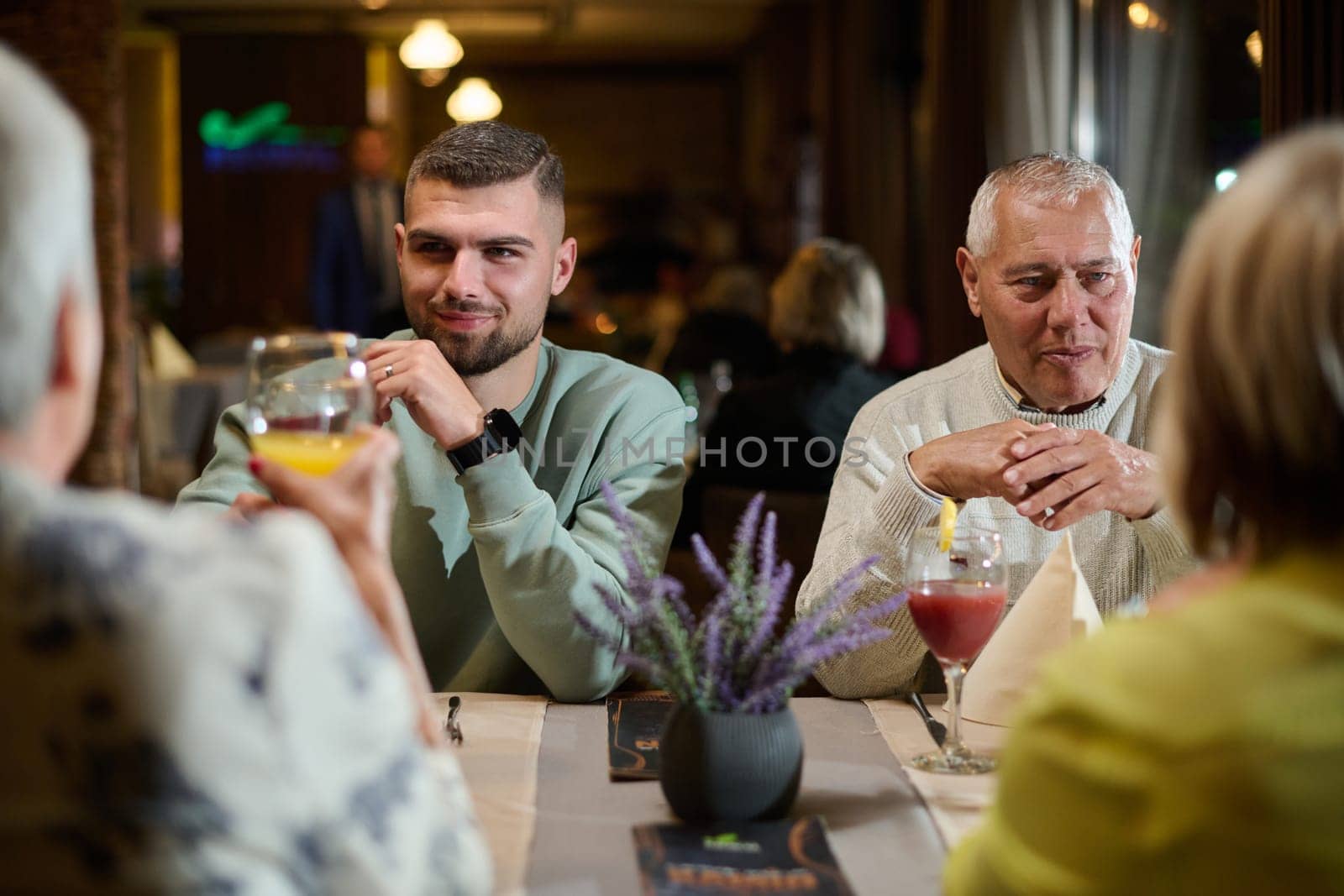 A group of family friends, comprising a young grandson and older individuals, share a delightful dinner in a modern restaurant, exemplifying the concept of healthy aging through intergenerational bonding and a joyous dining experience by dotshock