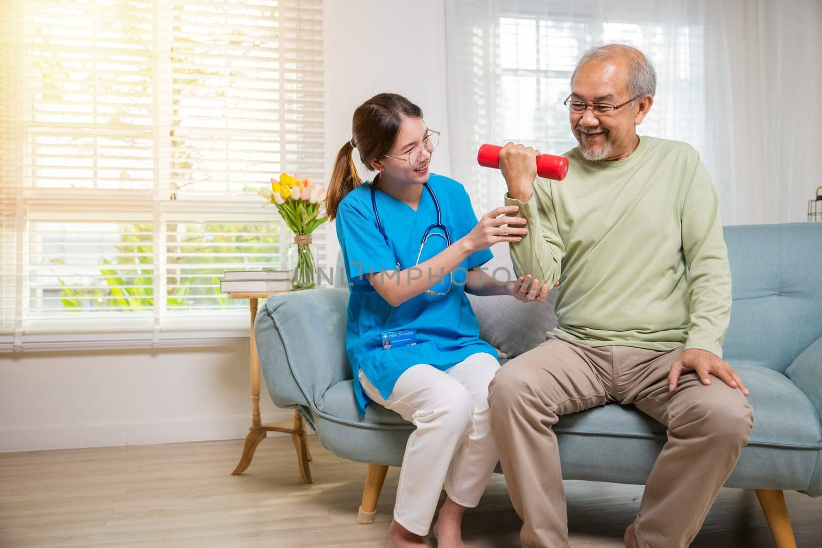 Asian nurse physiotherapist helping senior man in lifting dumbell at retirement home by Sorapop