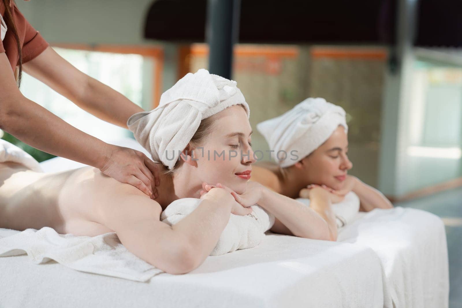 Couple of beautiful young woman lie on white spa bed during having back massage. Attractive caucasian woman having back massage at traditional spa room. Relaxing and healthy concept Tranquility.