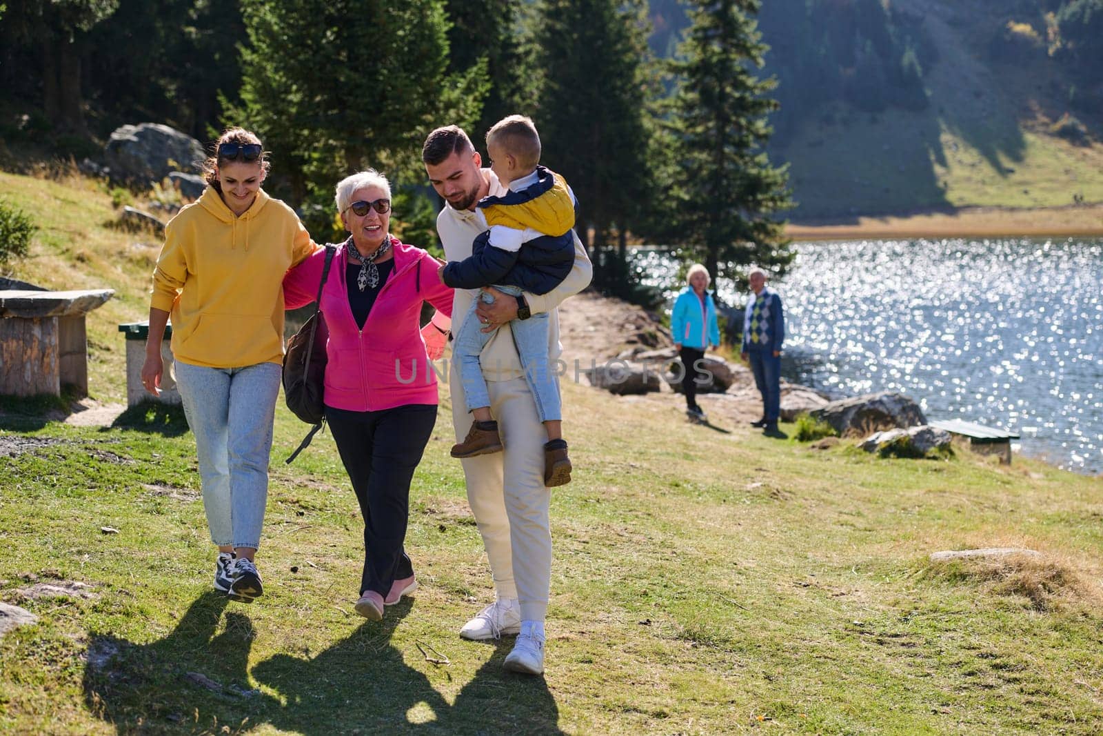 A family shares delightful moments with their friends amid the stunning landscapes of mountains, lakes, and winding paths, promoting a healthy lifestyle and the joy of familial bonds in the embrace of nature's beauty by dotshock