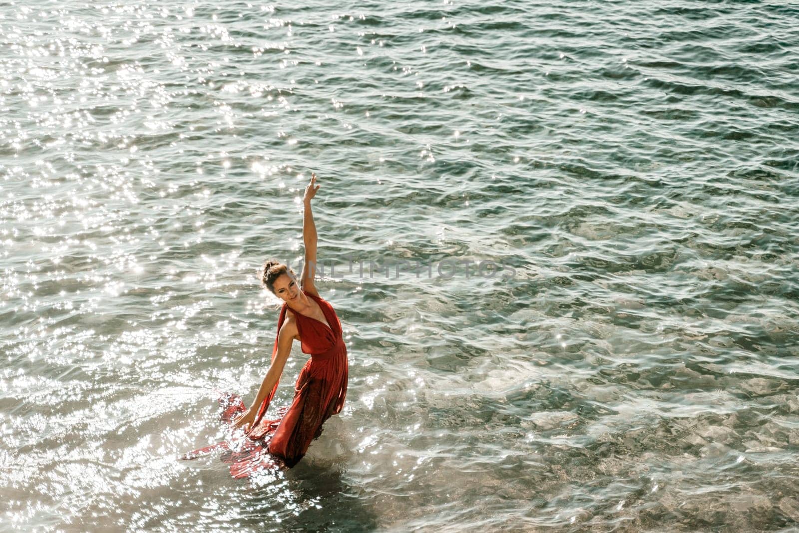 Woman red dress sea. Female dancer in a long red dress posing on a beach with rocks on sunny day.