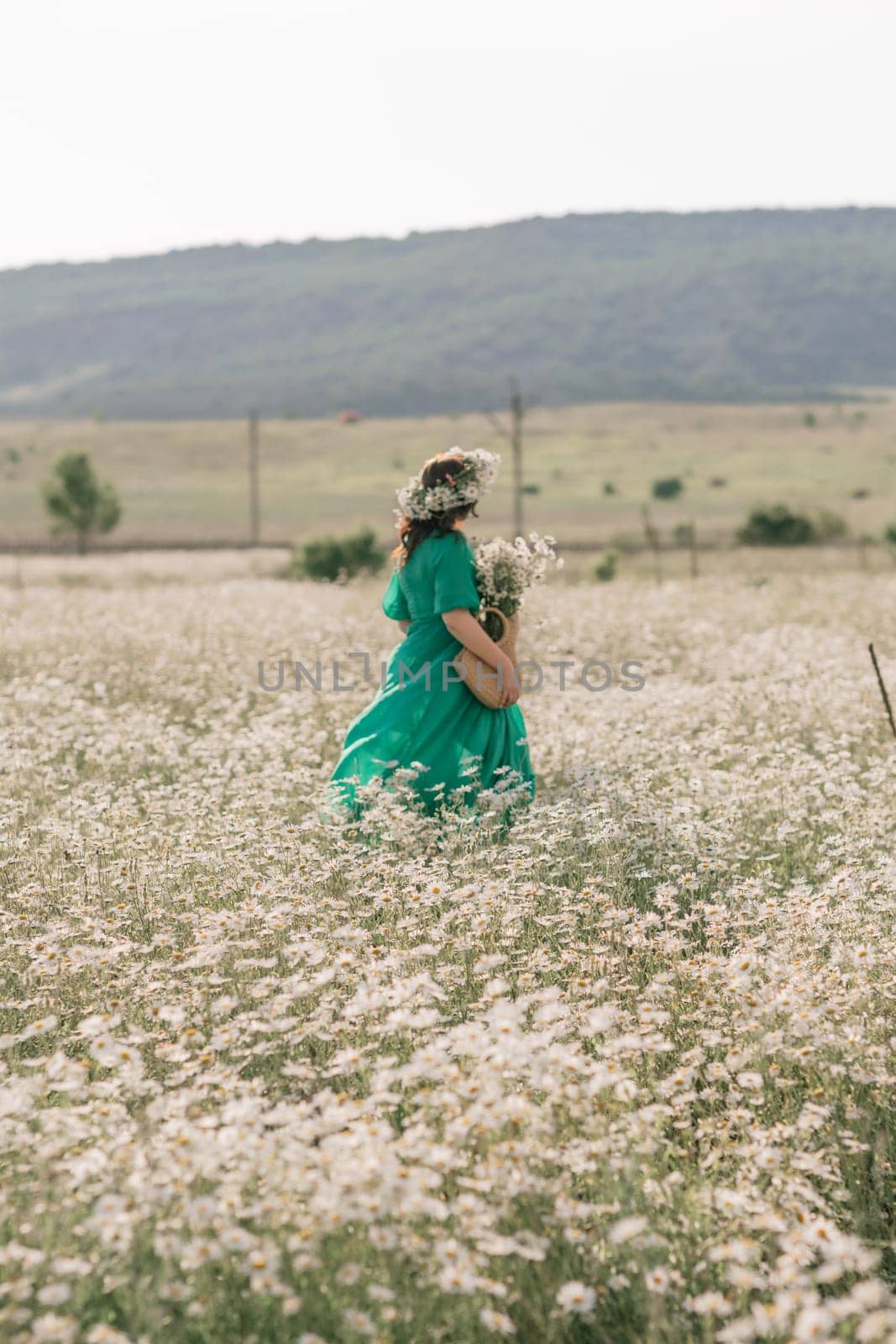 Happy woman in a field of daisies with a wreath of wildflowers on her head. woman in a green dress in a field of white flowers. Charming woman with a bouquet of daisies, tender summer photo by Matiunina