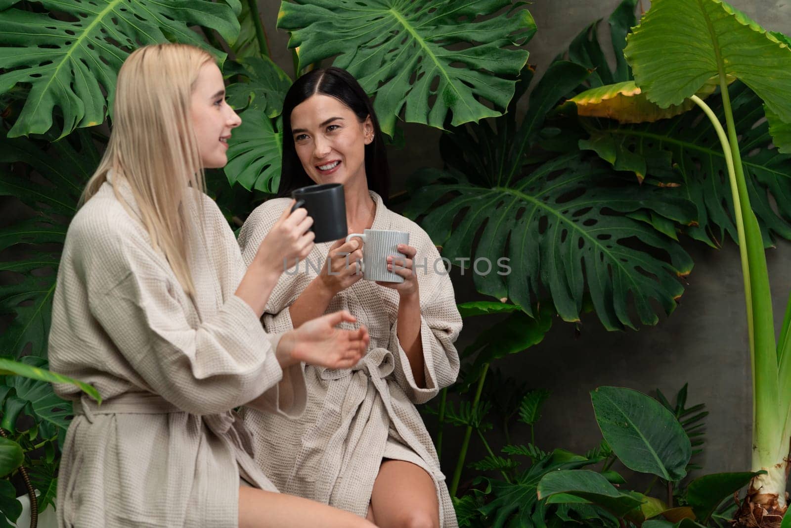 Tropical and exotic spa garden with bathtub in modern hotel or resort with young two women in bathrobe drink coffee, enjoy leisure and wellness lifestyle surround by lush greenery foliage. Blithe