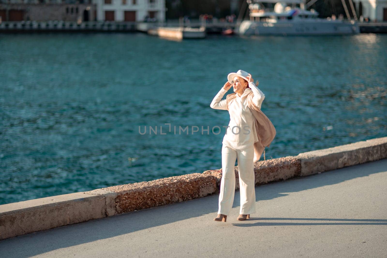 Happy blonde woman in a white suit and hat posing at the camera against the backdrop of the sea by Matiunina