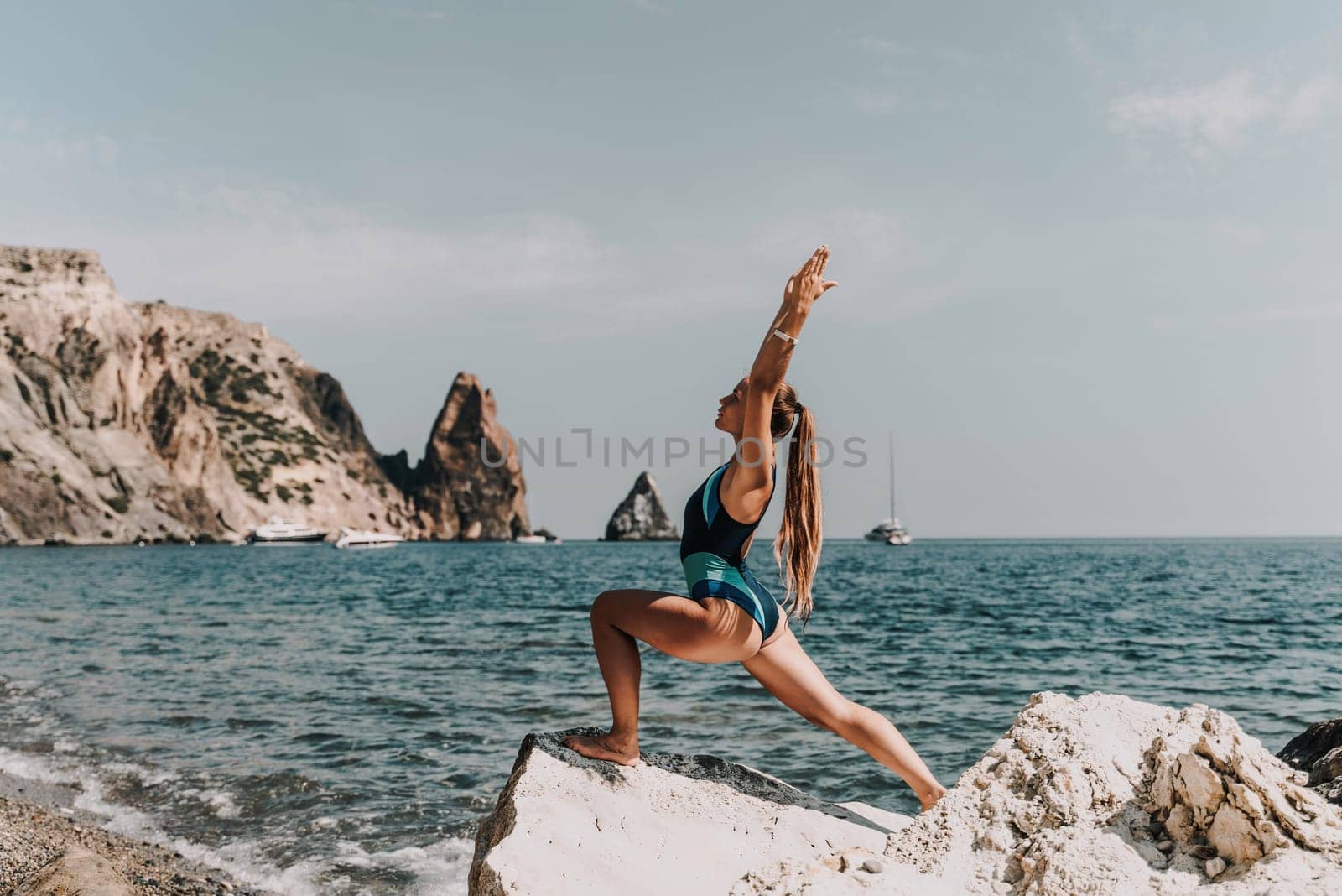 Yoga on the beach. A happy woman meditating in a yoga pose on the beach, surrounded by the ocean and rock mountains, promoting a healthy lifestyle outdoors in nature, and inspiring fitness concept