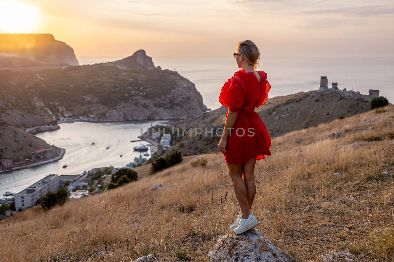 Happy woman standing with her back on the sunset in nature in summer with open hands posing with mountains on sunset, silhouette. Woman in the mountains red dress, eco friendly, summer landscape active rest by Matiunina
