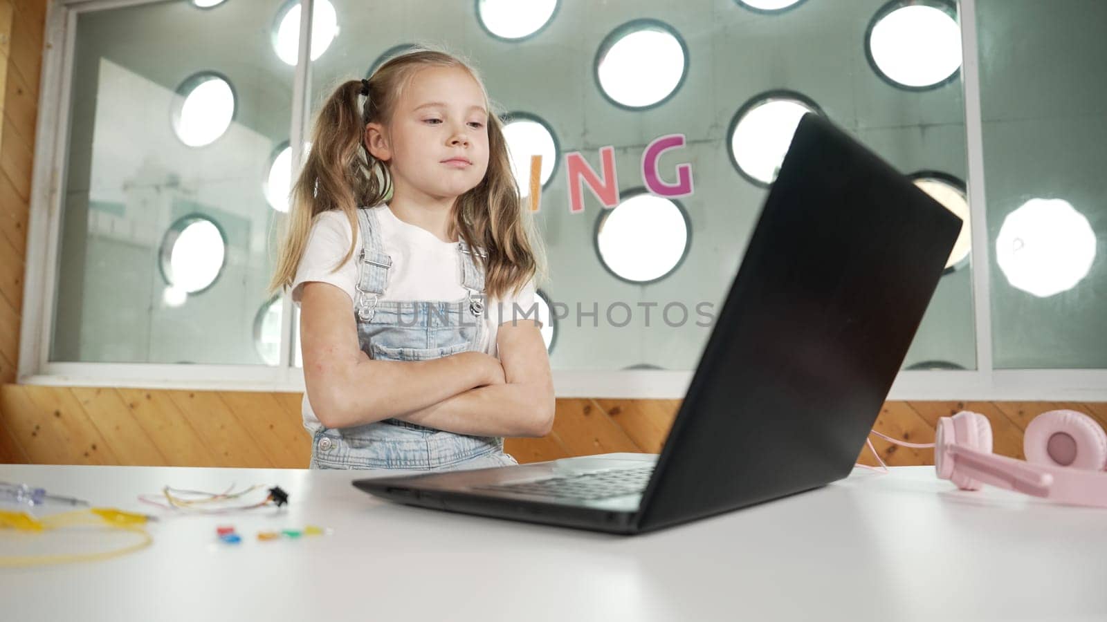 Caucasian girl using laptop programing software while crossing arms with confident to celebrate successful project. Pretty child coding system while looking screen proudly in Stem class. Erudition.