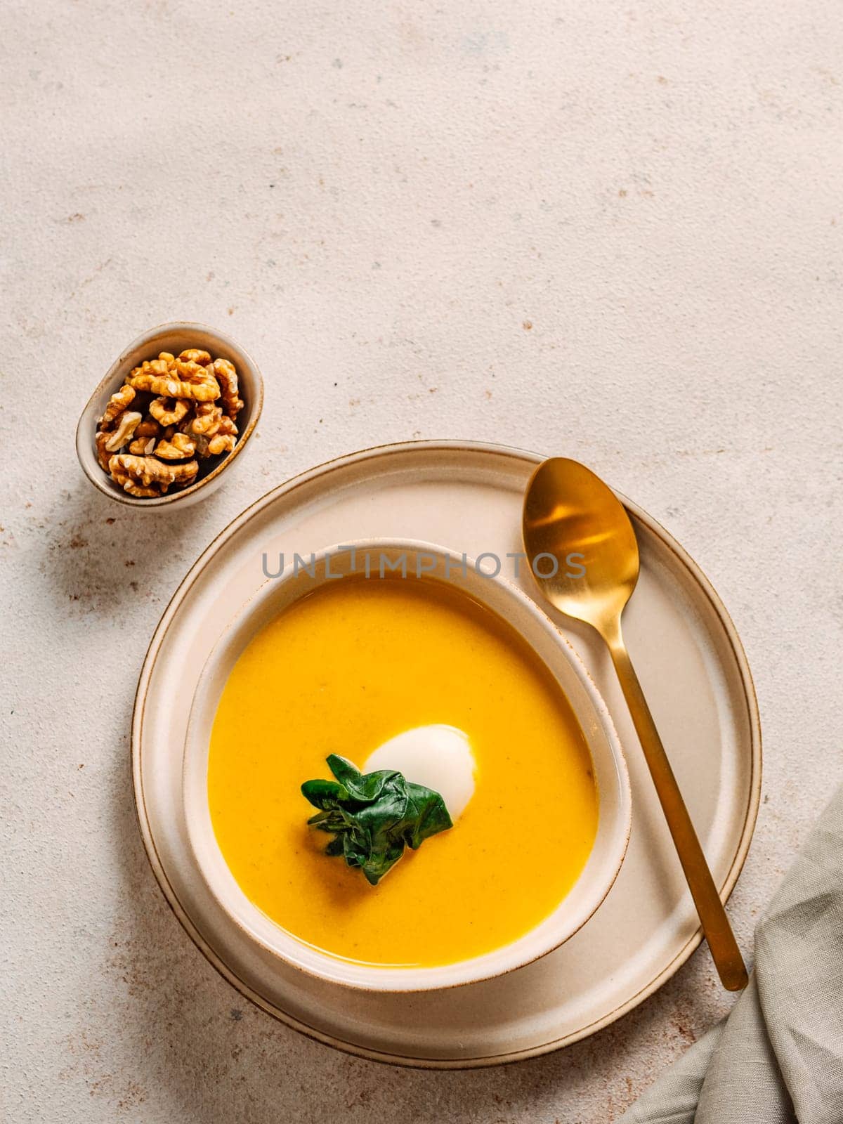 Pumpkin cream-soup served spinach. Tasty Homemade Pumpkin, Sweet Potato or Carrot Soup in Bowl on Neutral Pastel Background. Cozy autumn comfort food. Copy space, vertical. Top view