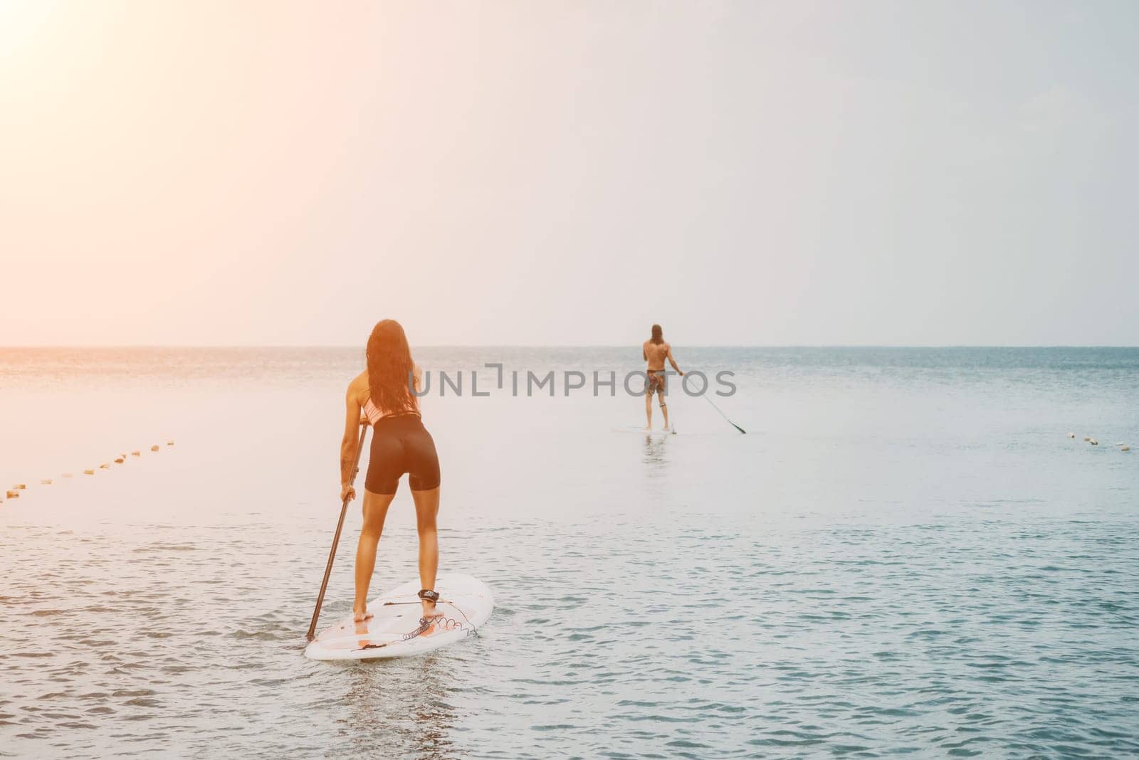 Sea woman and man on sup. Silhouette of happy young woman and man, surfing on SUP board, confident paddling through water surface. Idyllic sunset. Active lifestyle at sea or river