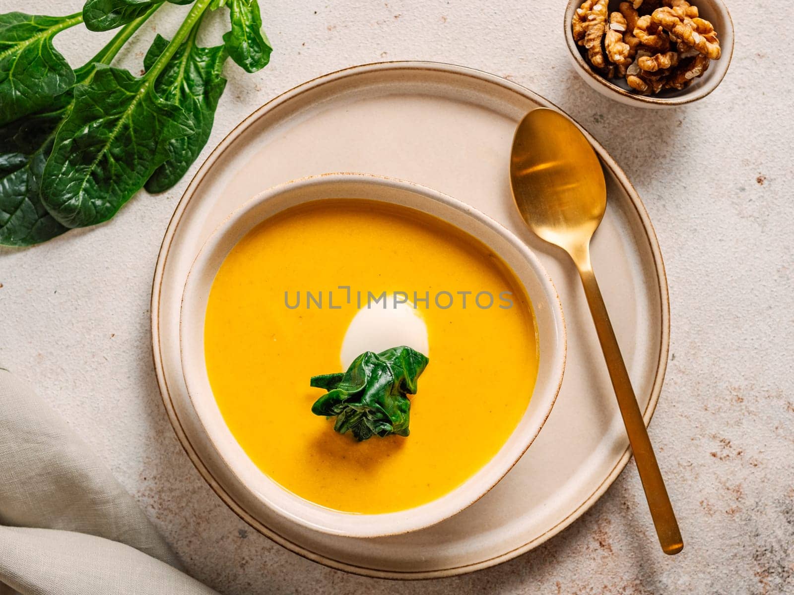 Pumpkin cream-soup served spinach, nuts, sour cream. Tasty Homemade Pumpkin, Sweet Potato or Carrot Soup in Bowl on Neutral Pastel Background. Cozy autumn comfort food. Top view