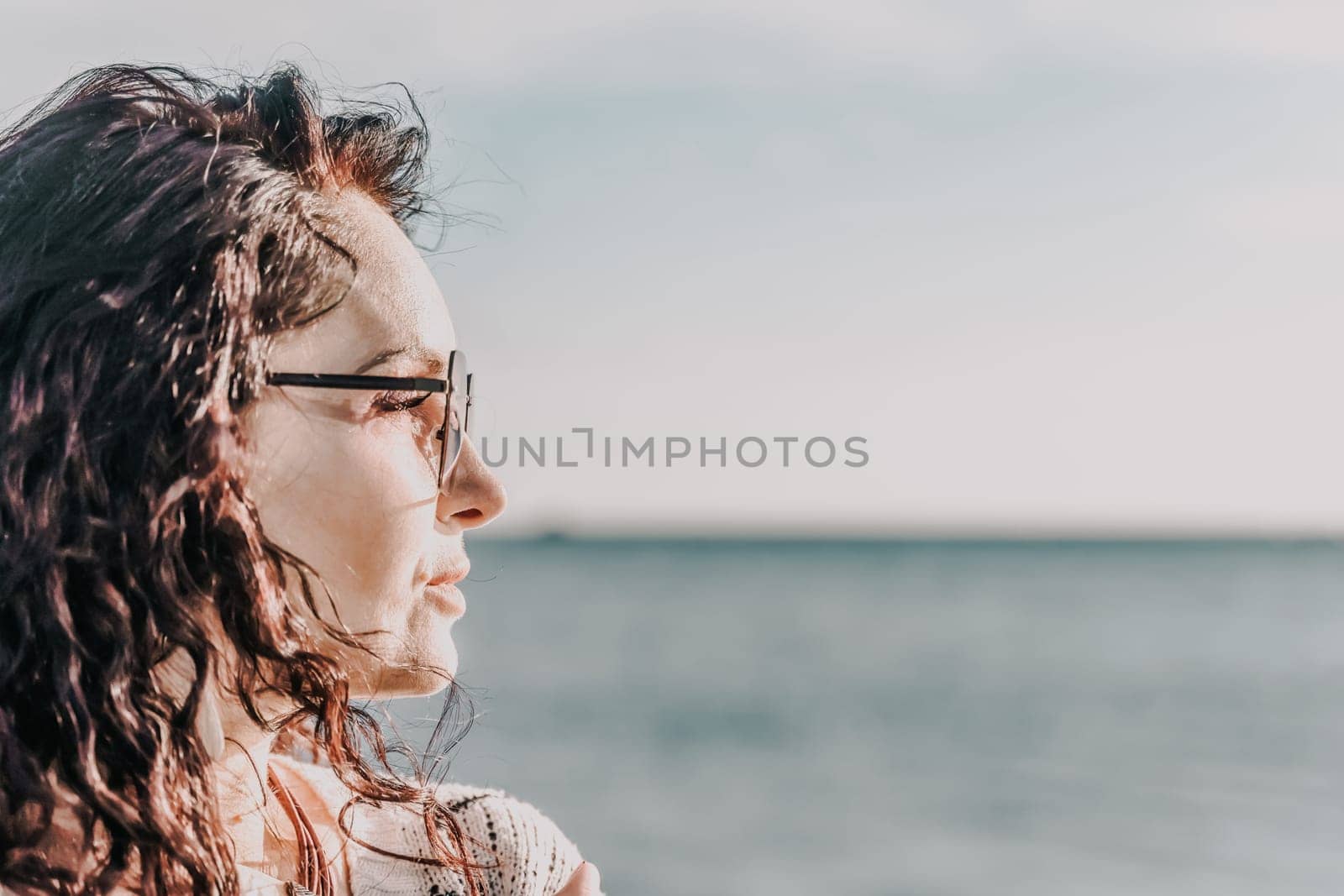 Portrait of a curly woman in glasses on the background of the se by Matiunina