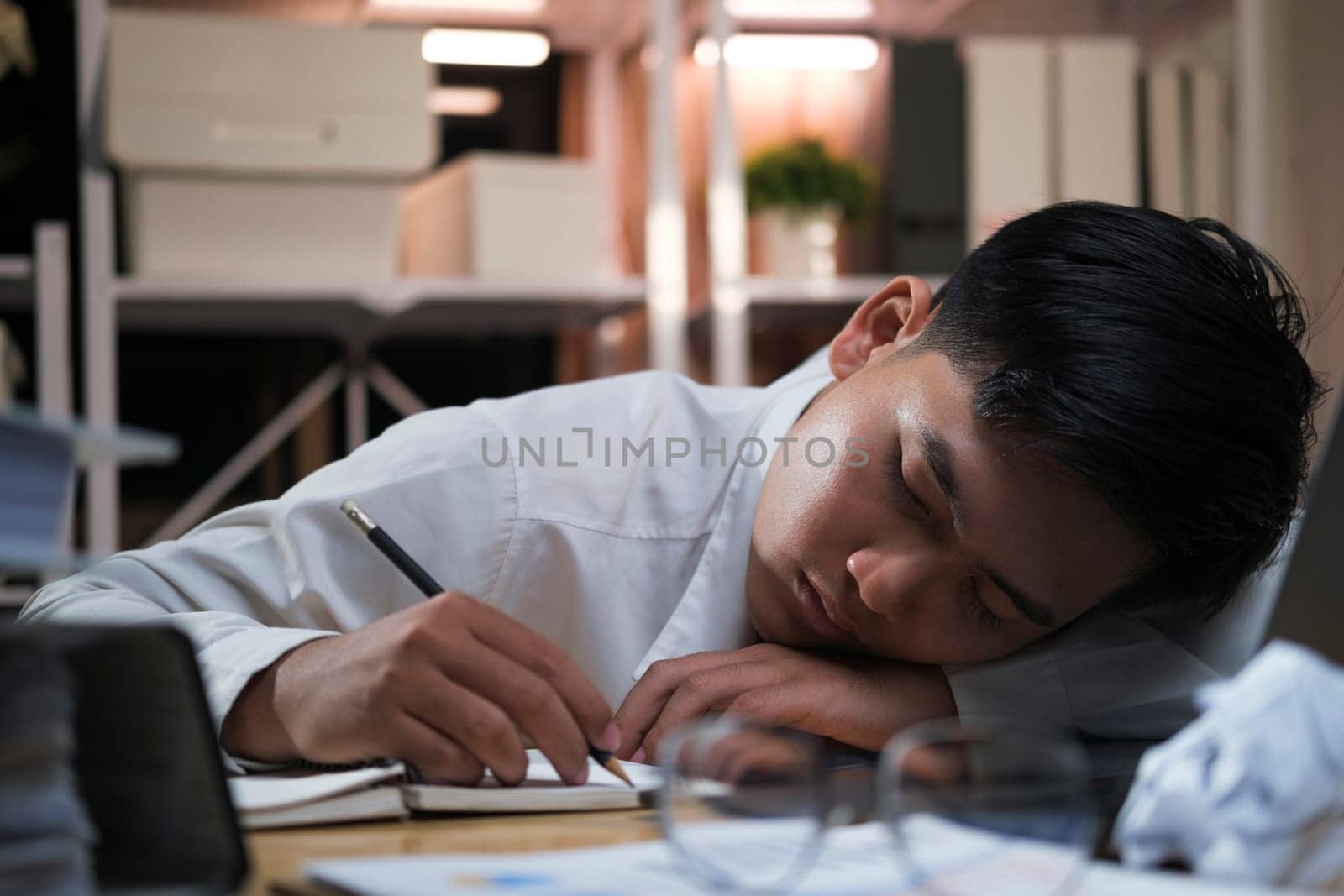 Exhausted businessman sleeping on his office desk, next to laptop and documents, tired of overworking.