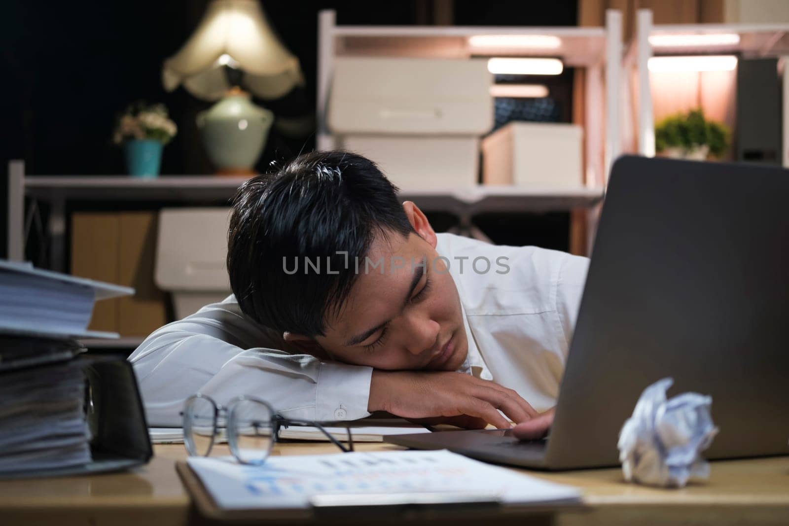 Young tired businessman lying on table at night office.. by ijeab