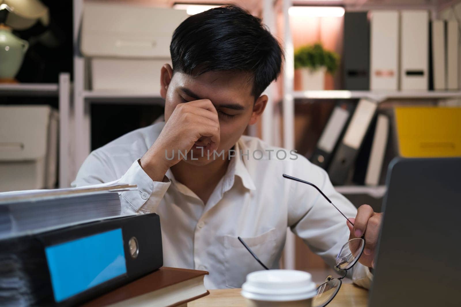 Asian young tired staff businessman using desktop computer having overwork project overnight in office, exhausted unhappy businessman feeling sleepy after after working hard overtime at night.