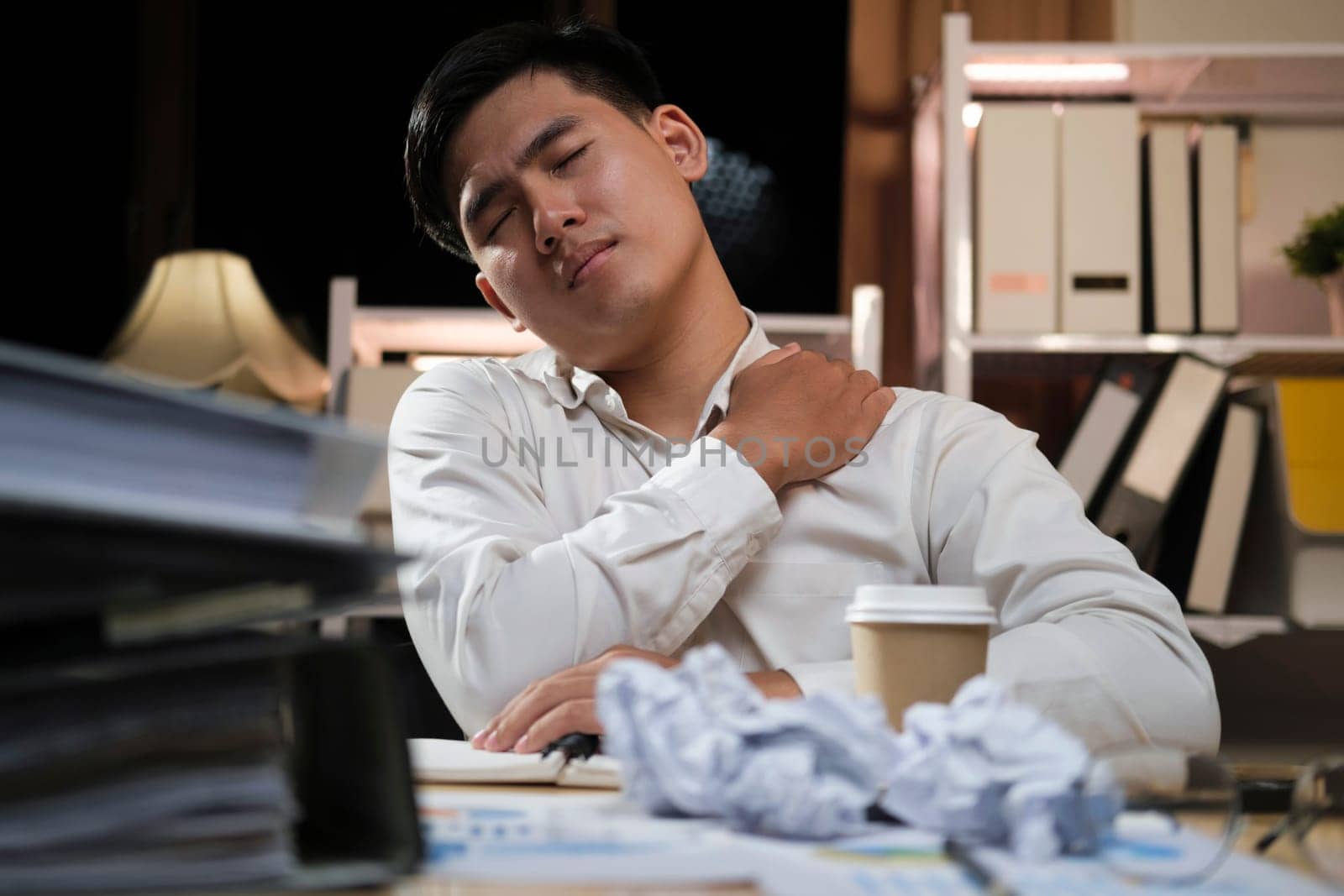 Asian businessman overtime work and feel shoulder pain in the office feeling tired, fatigue, exhausted while working overtime at night in office.