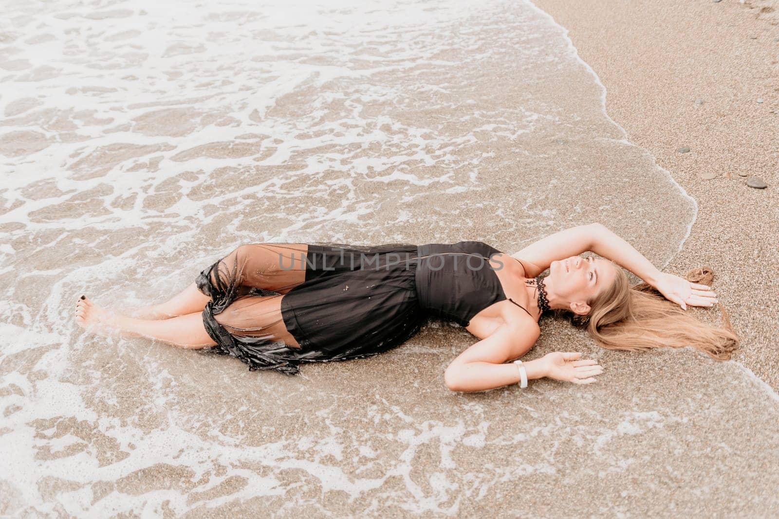 Woman summer travel sea. Happy tourist in black dress enjoy taking picture outdoors for memories. Woman traveler posing on sea beach surrounded by volcanic mountains, sharing travel adventure journey by panophotograph