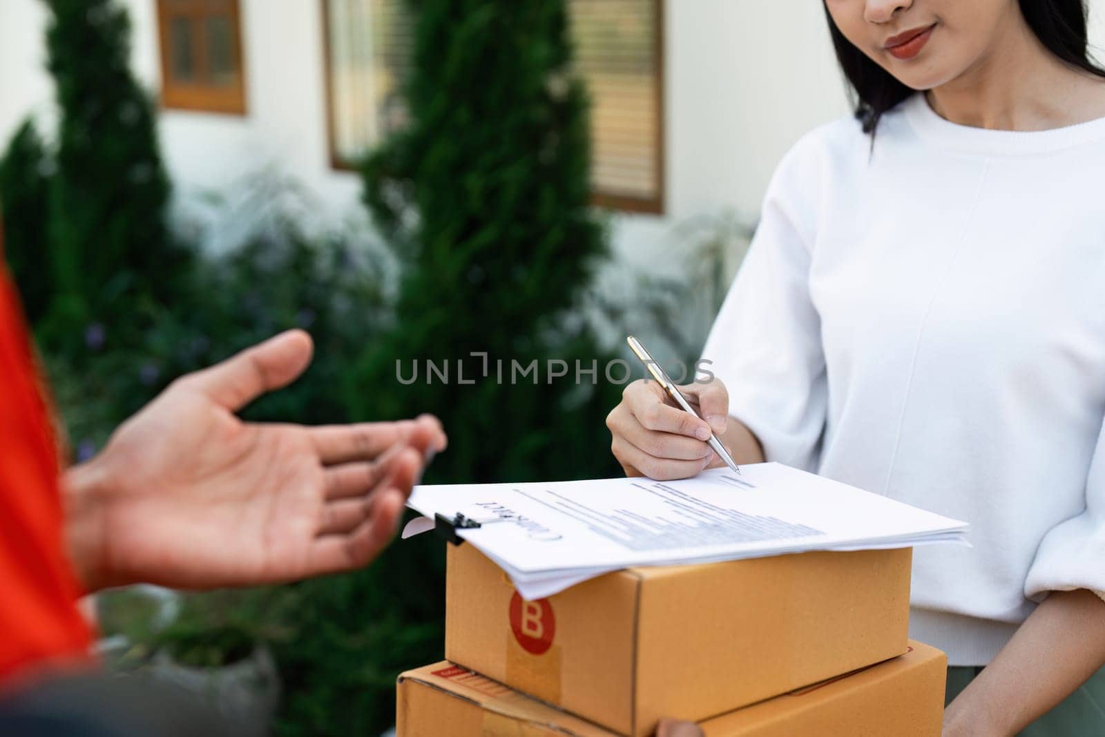 Young woman signature in document to receive package from professional delivery man at home.