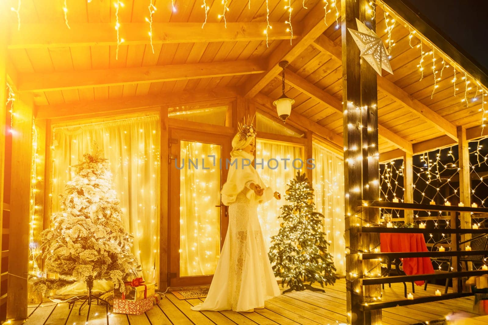 Happy smiling woman in a white dress holding a gift box in front of a Christmas tree. by panophotograph