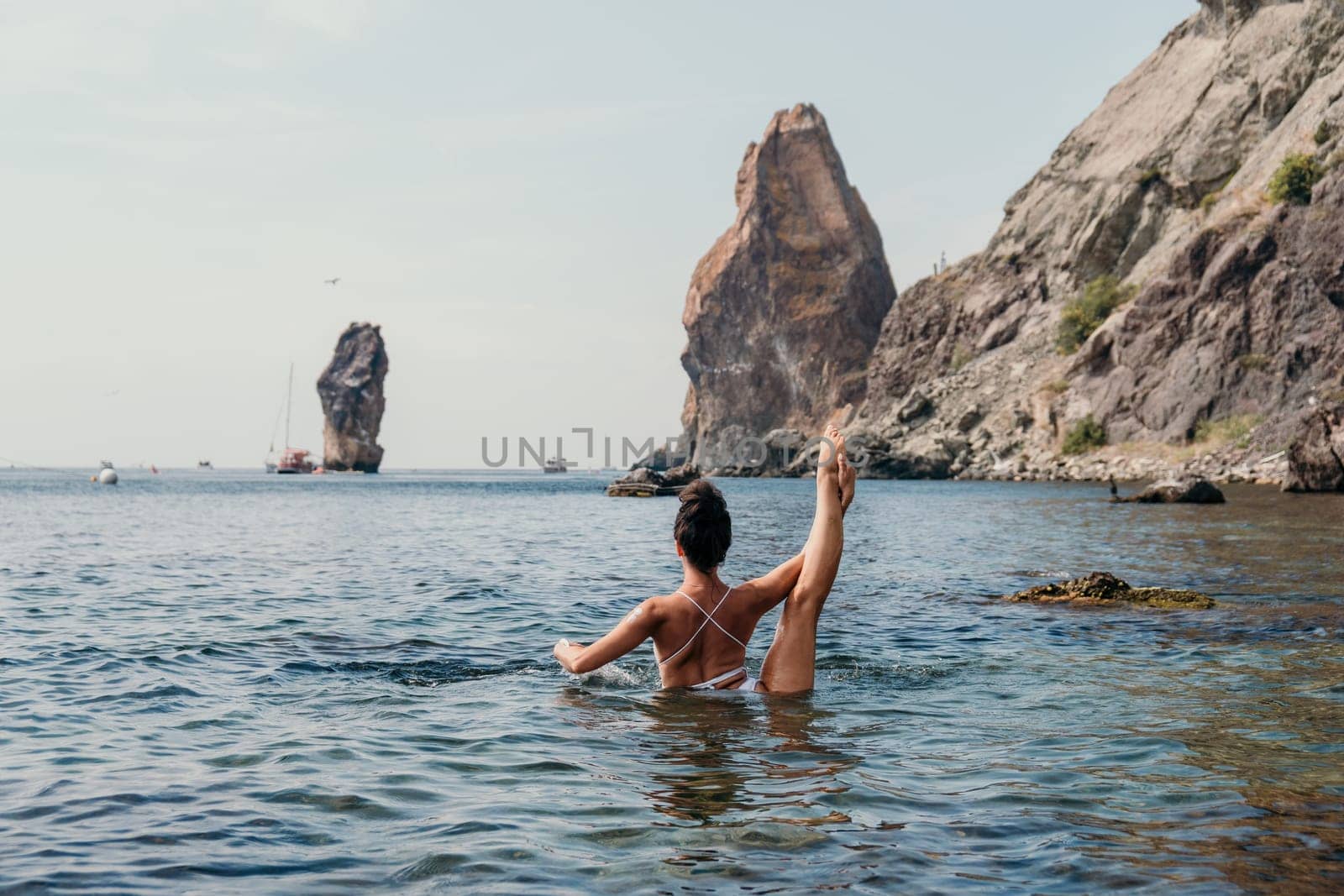 Young woman with black hair, fitness instructor in pink sports leggings and tops, doing pilates on yoga mat with magic pilates ring by the sea on the beach. Female fitness daily yoga concept