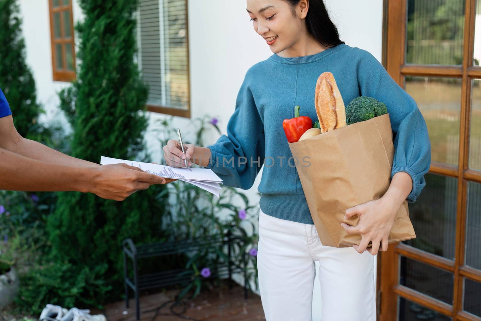 Asian woman signing the receipt on the order receipt through the online supermarket's home store.
