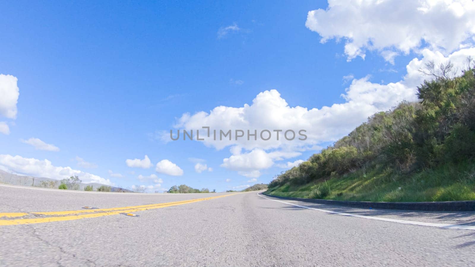 On a clear winter day, a car smoothly travels along Highway 101 near Santa Maria, California, under a brilliant blue sky, surrounded by a blend of greenery and golden hues.