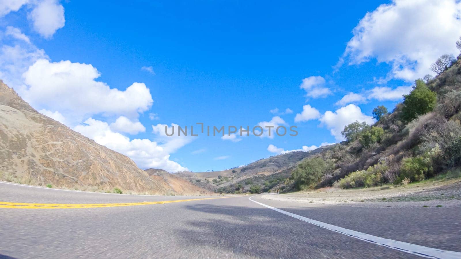 Vehicle is cruising along the Cuyama Highway under the bright sun. The surrounding landscape is illuminated by the radiant sunshine, creating a picturesque and inviting scene as the car travels through this captivating area.