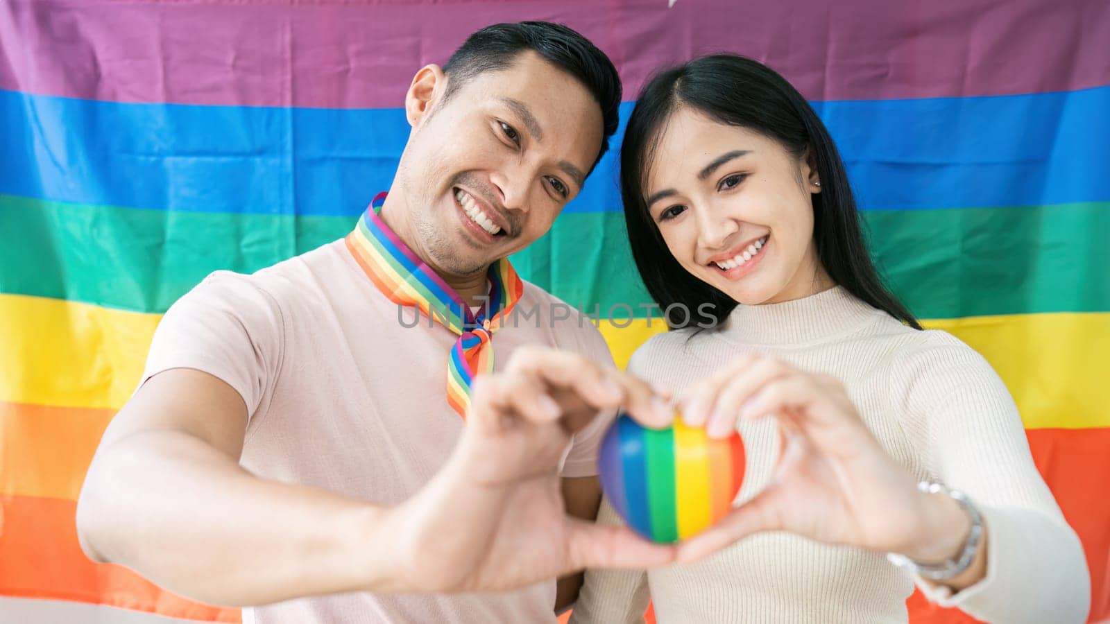 Gay and lesbian friend hold heart together with rainbow flag in background. lgbtq concept.