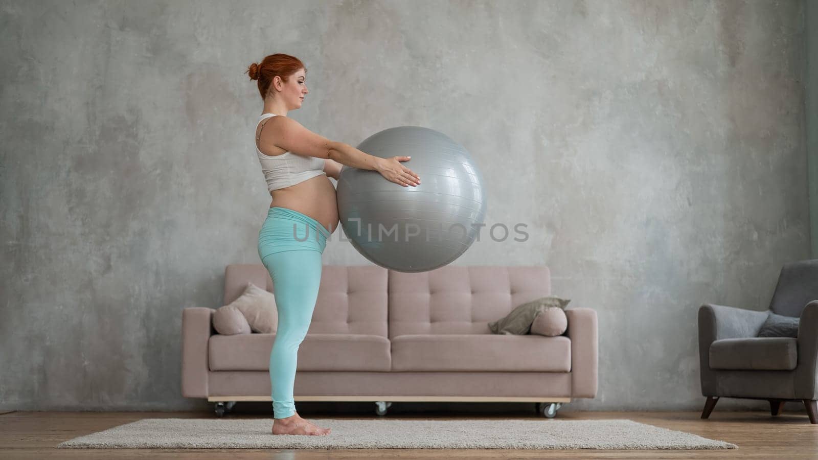 Pregnant red-haired woman doing arm exercises with fitball at home. by mrwed54