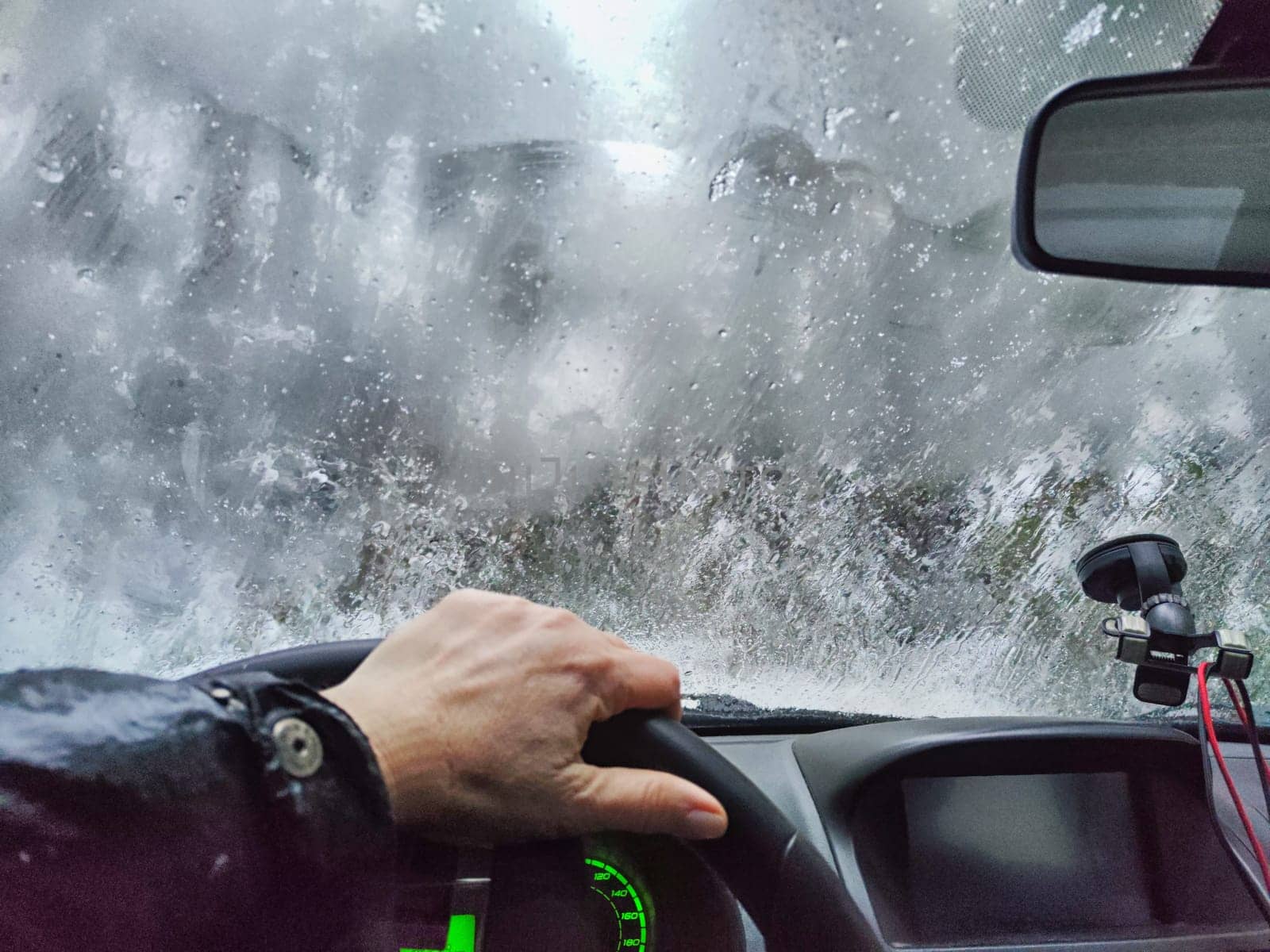 Hand of woman on steering wheel in car and and forest with cloudy windshield, fogged with snow ice in winter. Blurred woman driving car in travel