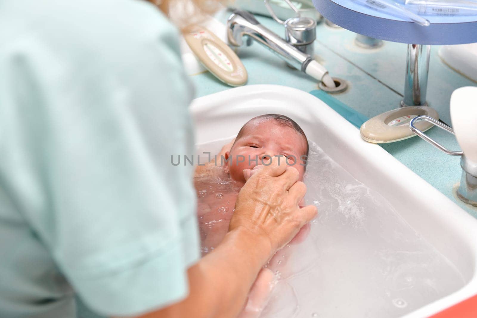 A nurse gives the first bath of a newborn boy by Godi