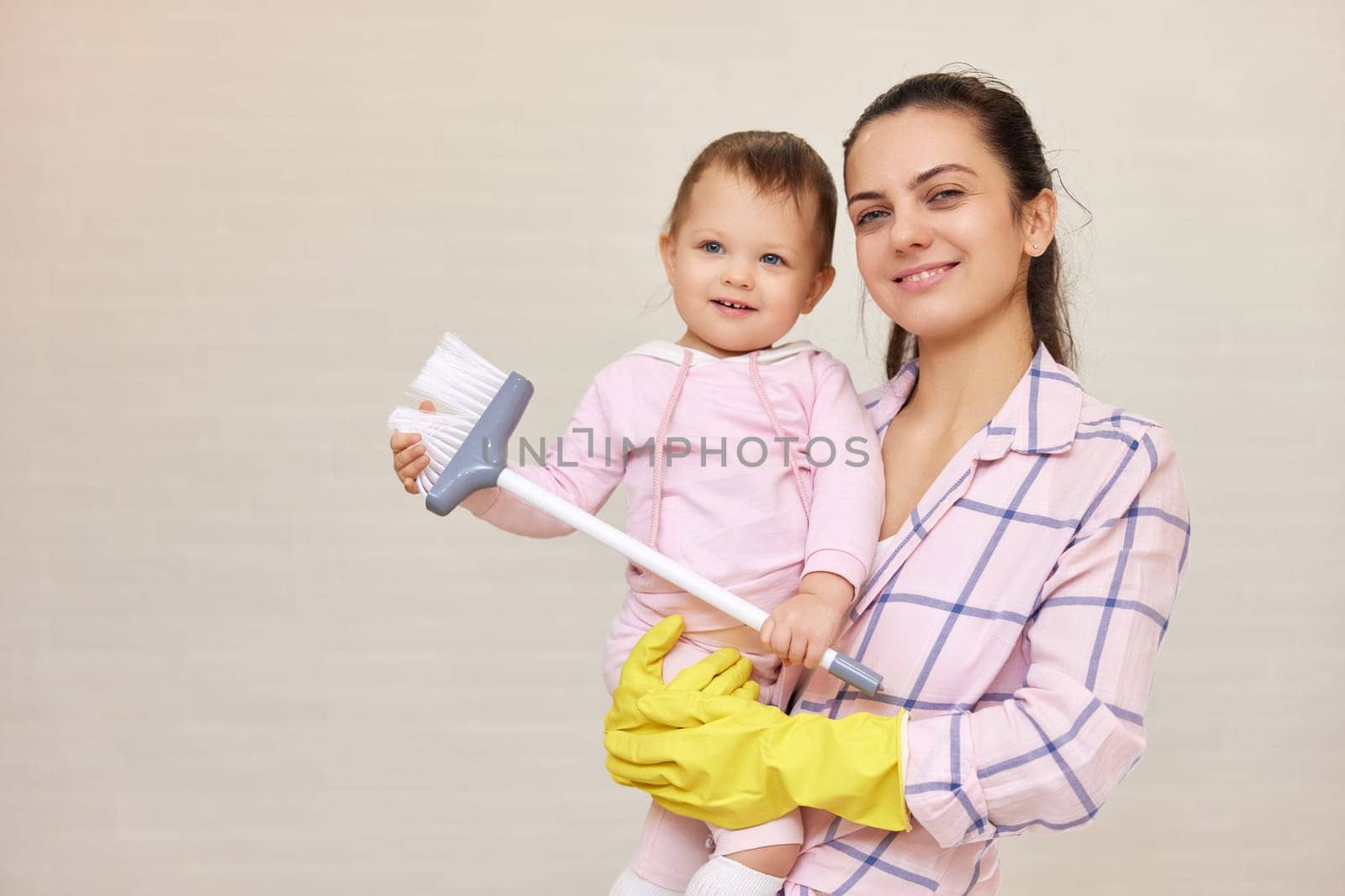 smiling mother housewife is holding cute baby kid and doing housework at home, Happy family, copy space