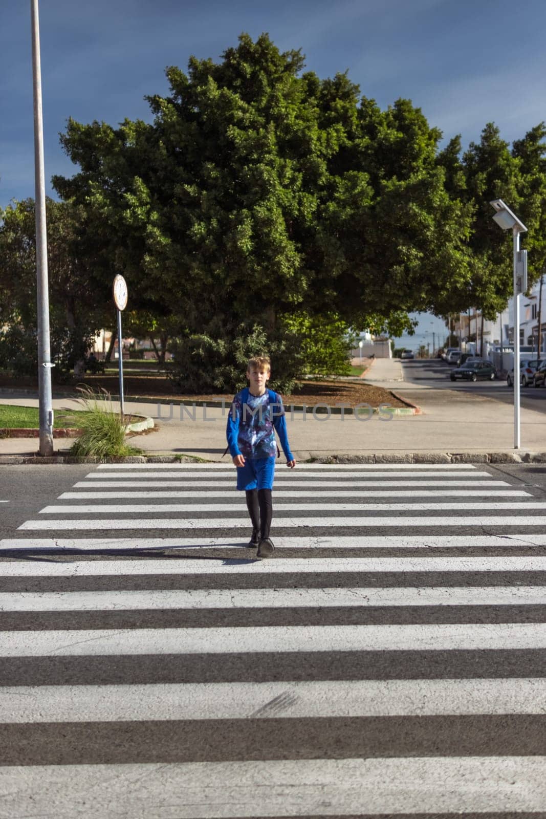 vertical photo child walks along the pedestrian crossing to the playground. Schoolboy with back bag. by PopOff