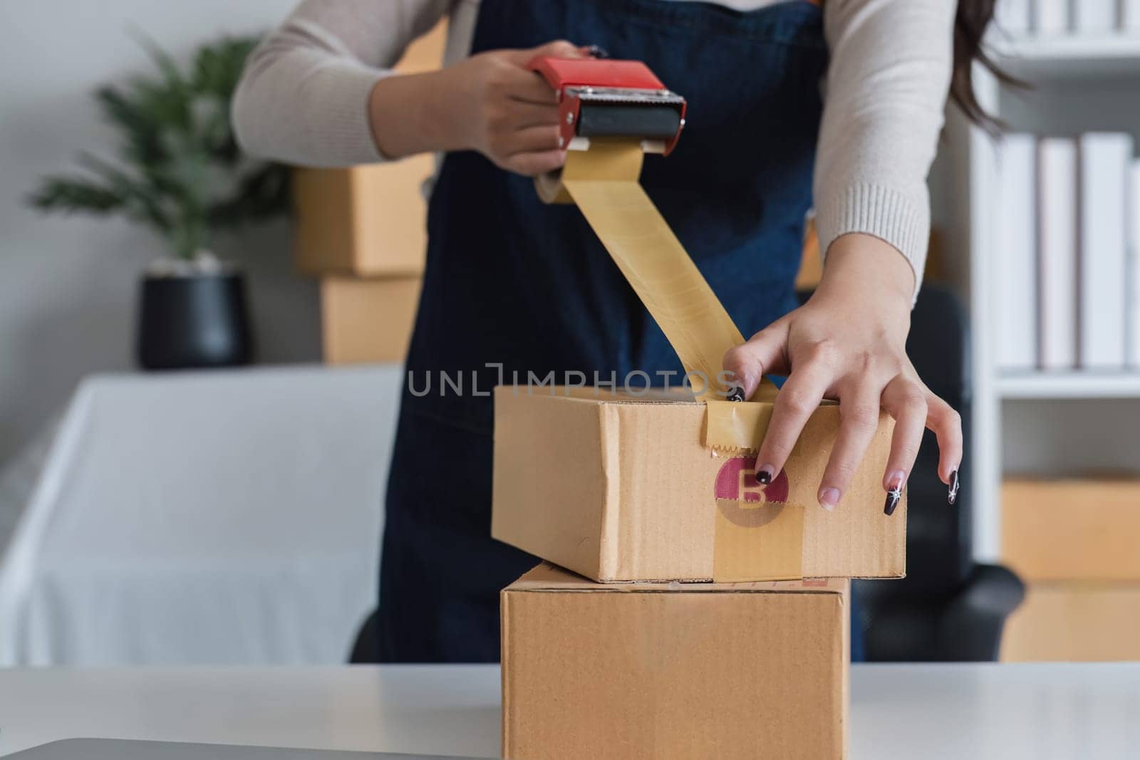 Young asian woman taping up a cardboard box in home office SME e-commerce business, relocation and new small business concept, SME concept by wichayada