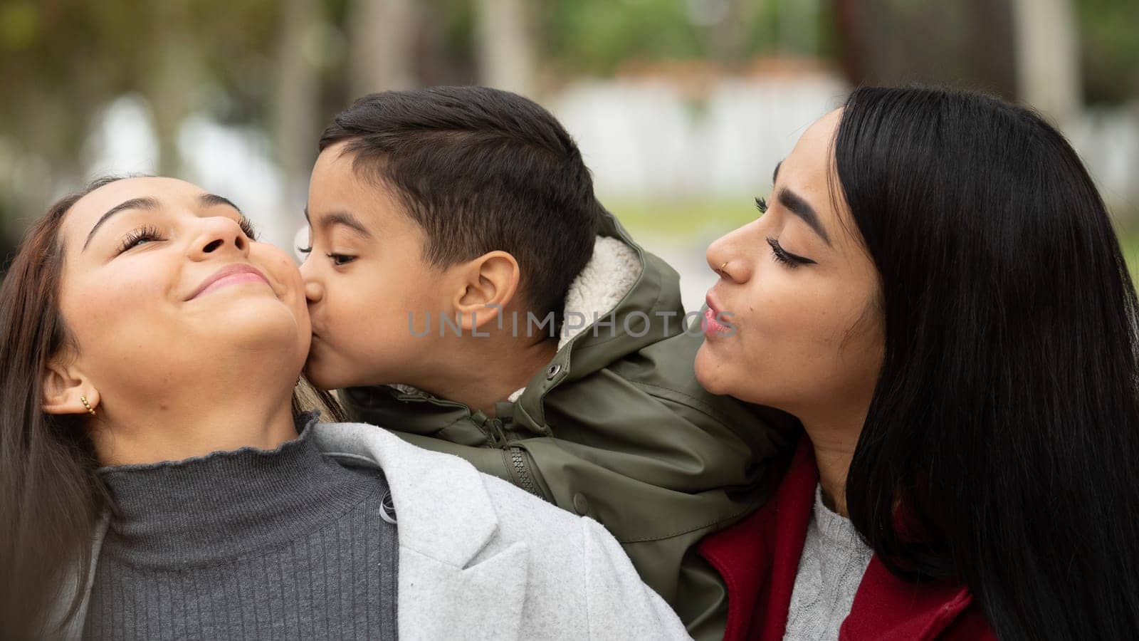 Outdoor family portrait of two lesbian women with their son who is kissing and showing love to his mom. LGBT concept.