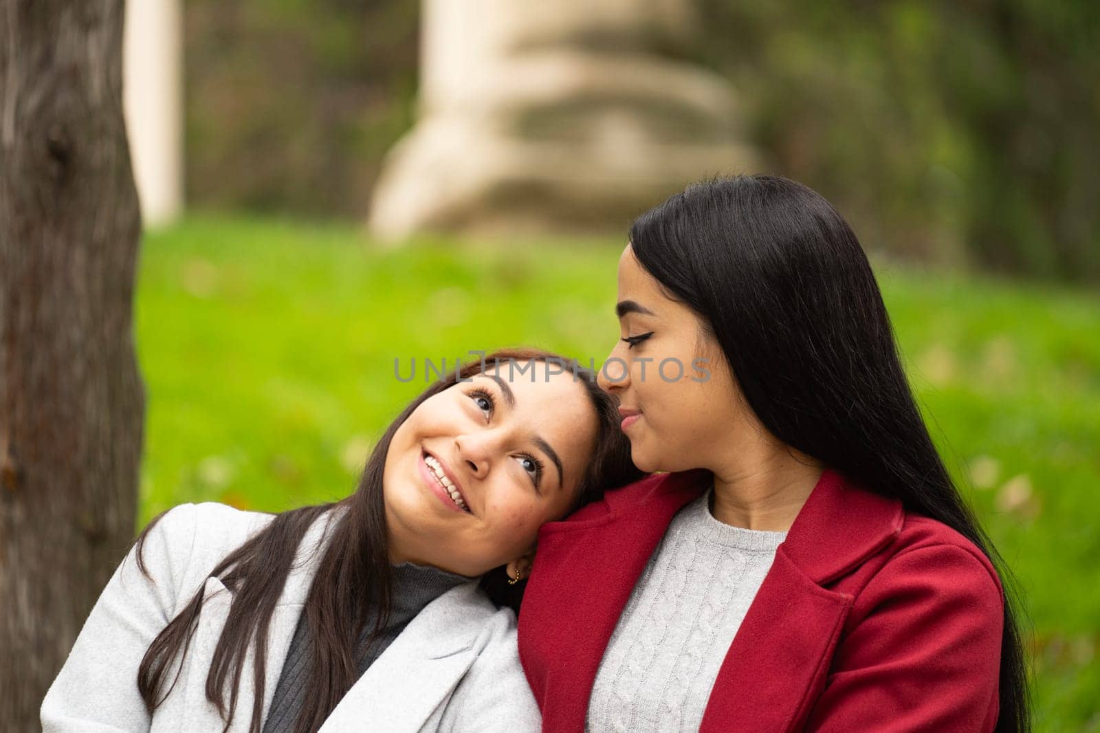 Portrait of smiling lesbian latin women relaxed together outdoors sitting on the grass by papatonic