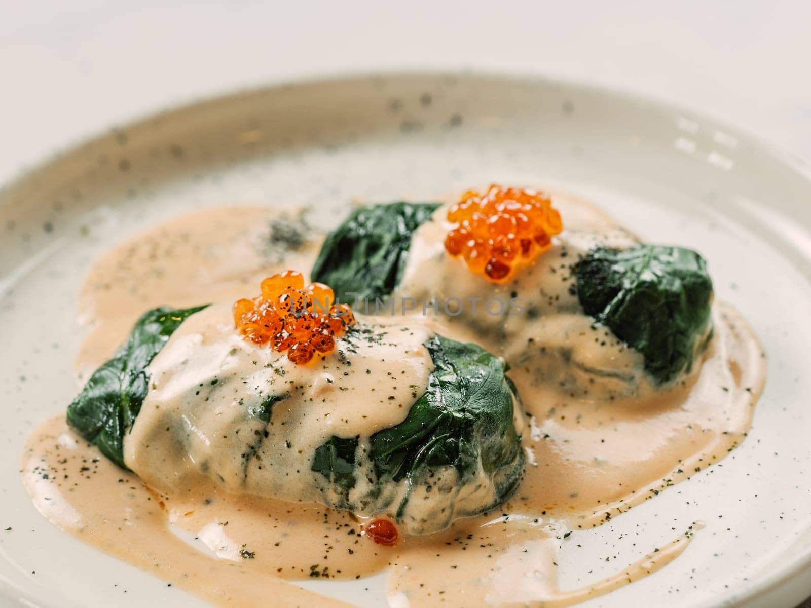 Stuffed green cabbage rolls with sauce in restaurant-style plating, served red caviar