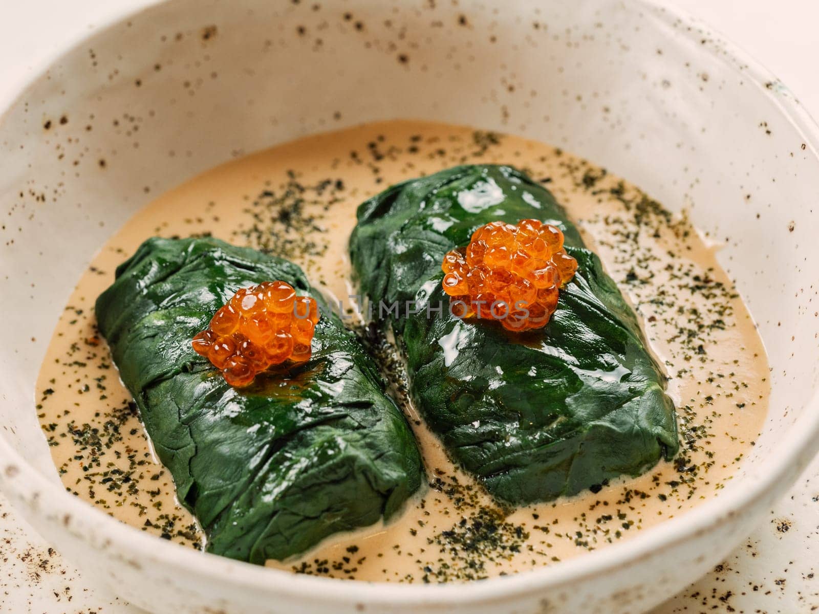 Stuffed green cabbage rolls with sauce in restaurant-style plating, served red caviar