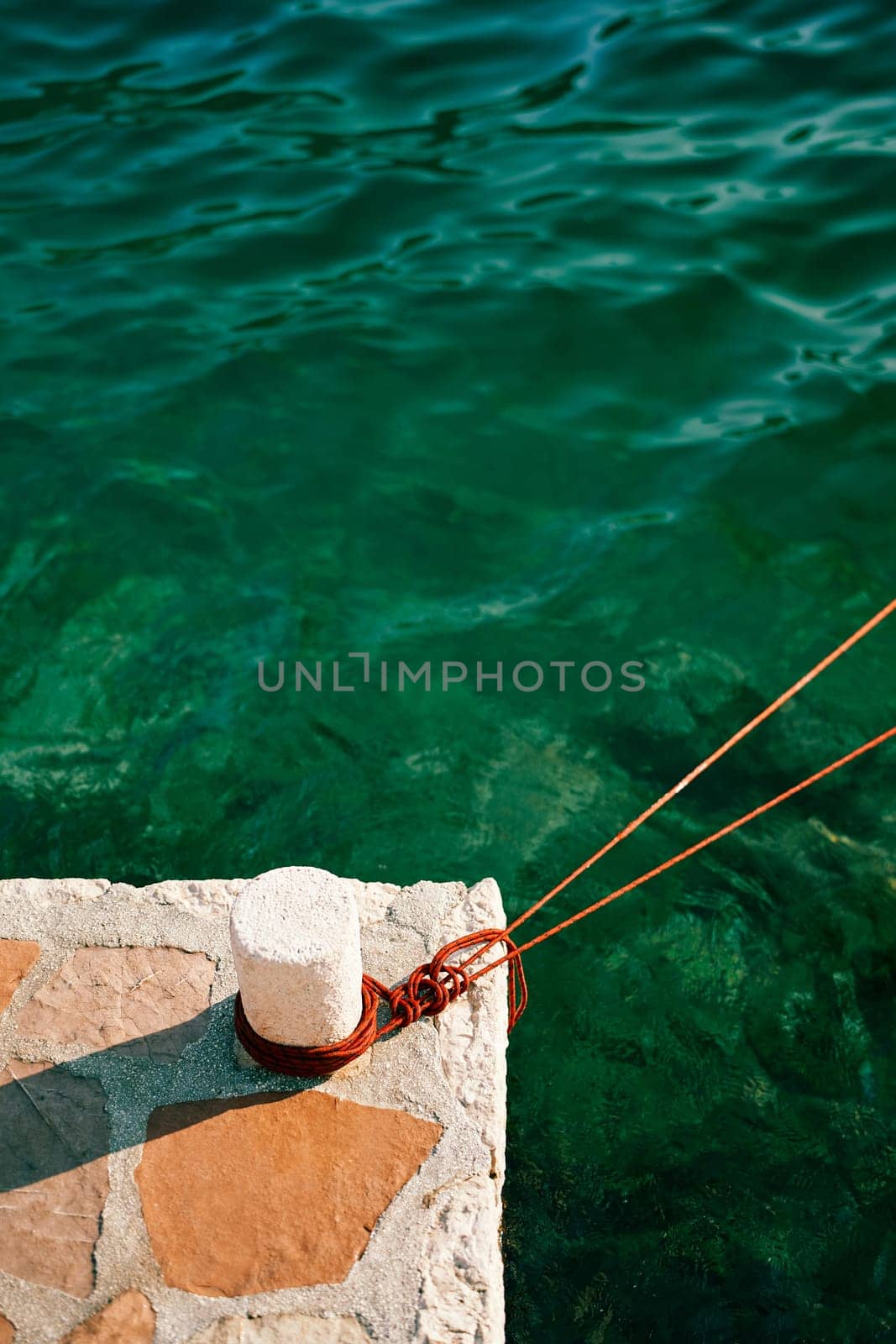 Rope wrapped around a bollard on a pier stretches over the sea. High quality photo