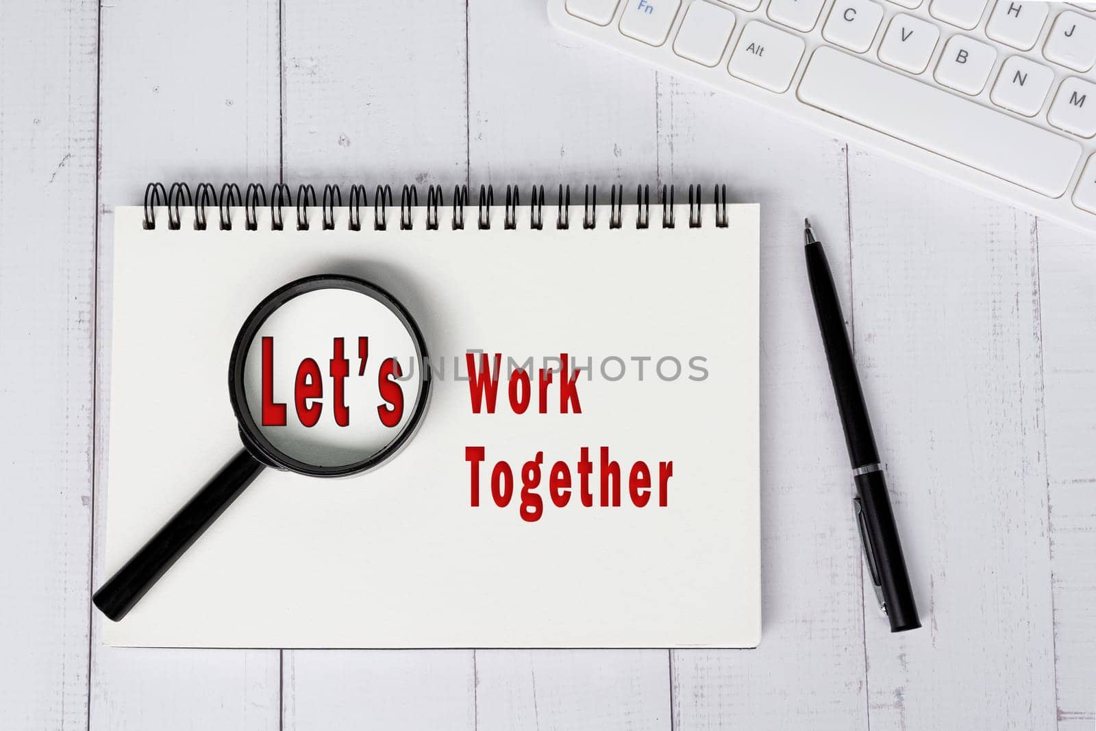 LET'S WORK TOGETHER text with magnify glass on note book on white wooden desk. Team work concept.